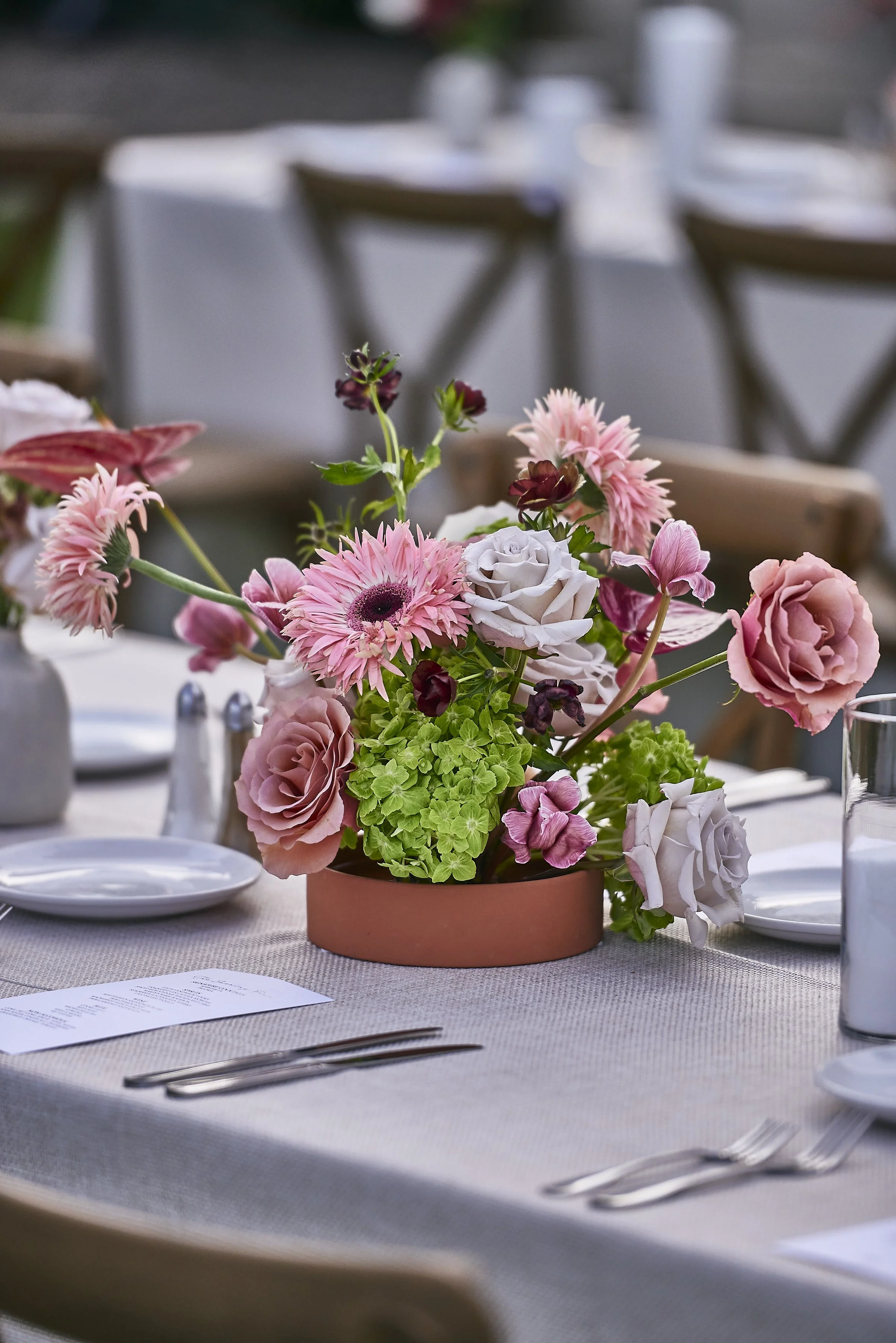 A floral centerpiece with pink, white, and burgundy flowers on a dining table set for a formal event.