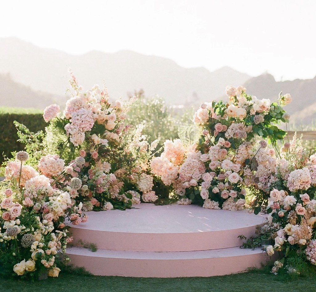 A floral stage with pink and white flowers, set outdoors with mountains in the background.