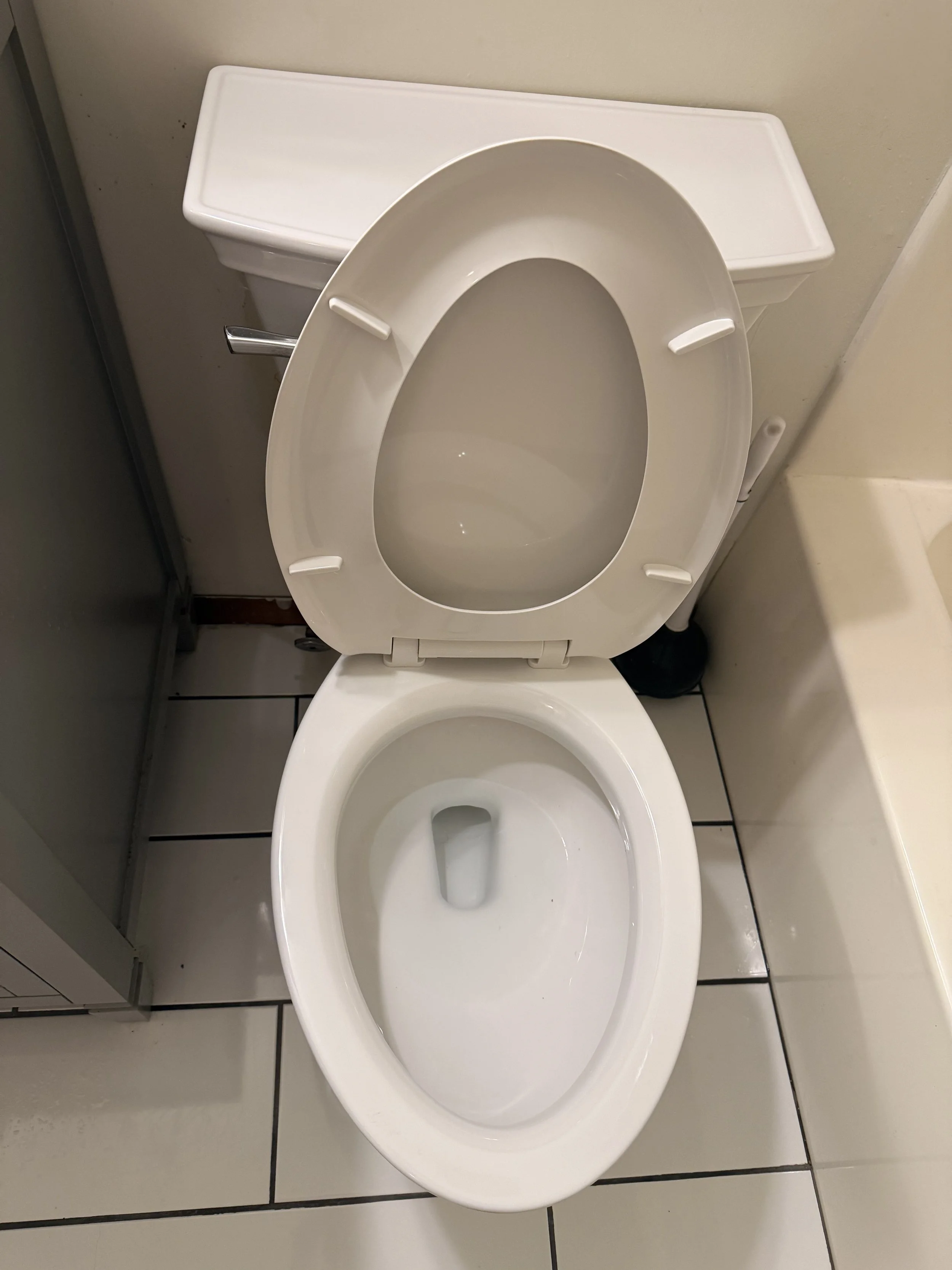 A white toilet with the lid up, situated in a tiled bathroom