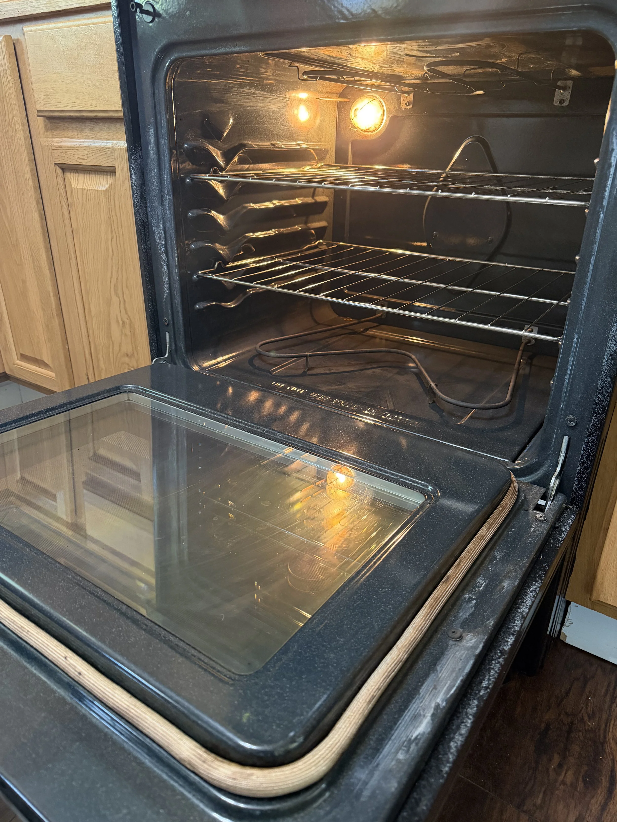 Inside a clean oven with lights on, empty oven racks, and a glass door with a metal handle.