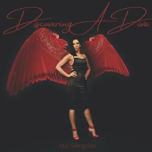 A woman standing with red angel wings, wearing a black dress and red high heels, against a black background with the text 'Discovering A Diva' and 'Mia GiAngelos'.
