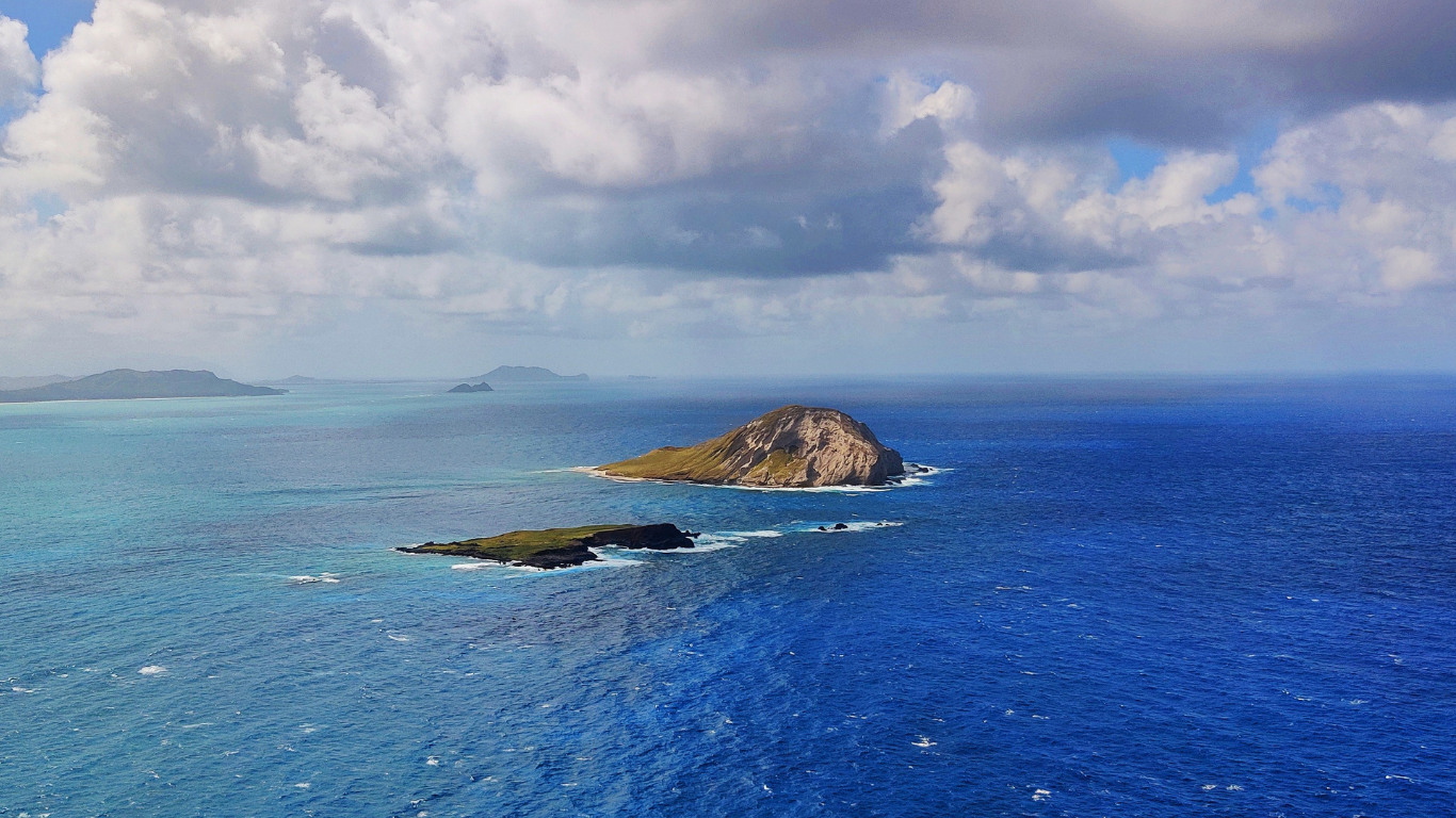 Aerial view of small islands in the ocean, with cloudy sky overhead.