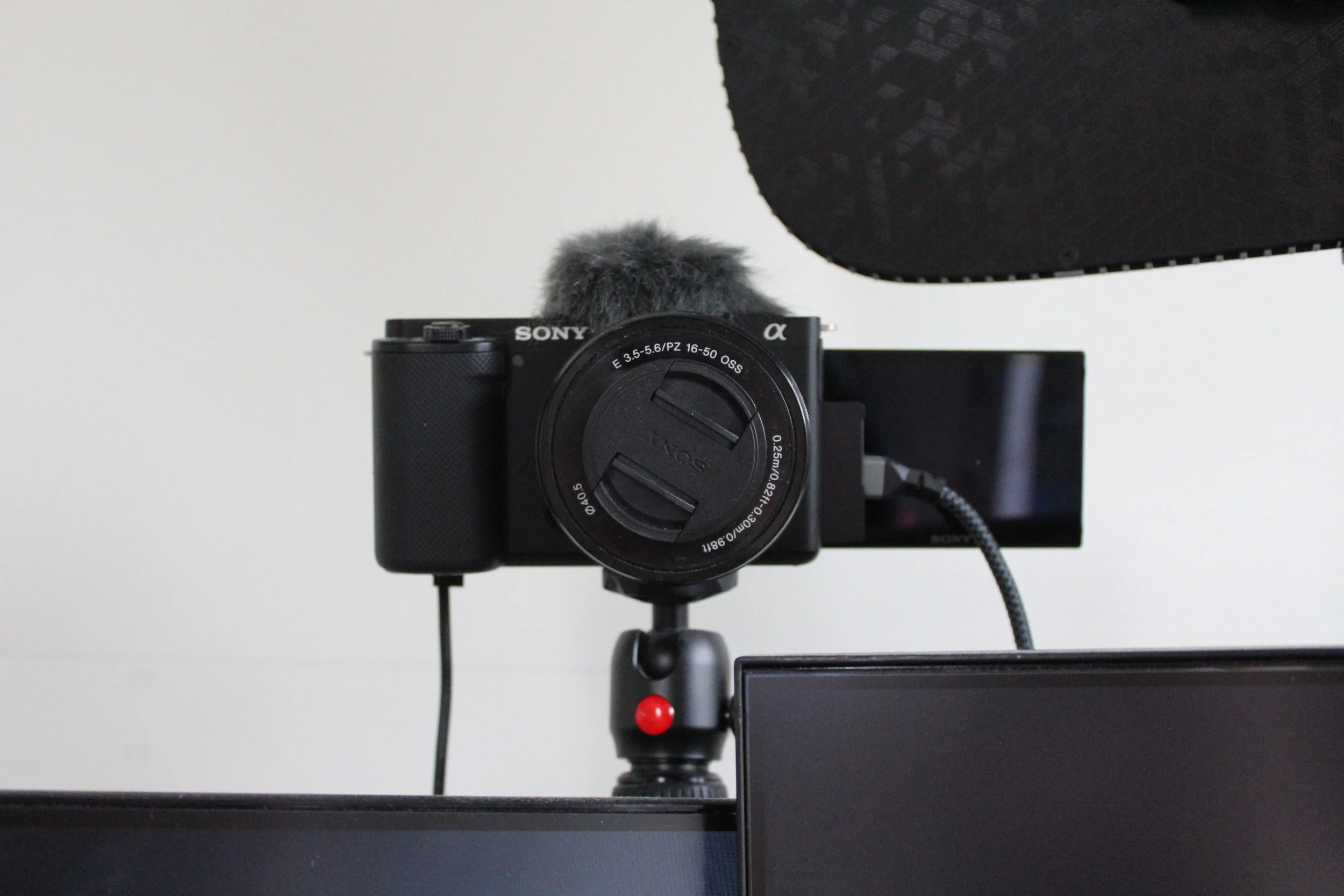 A camera mounted on a tripod with a microphone attached on top, facing a white wall.