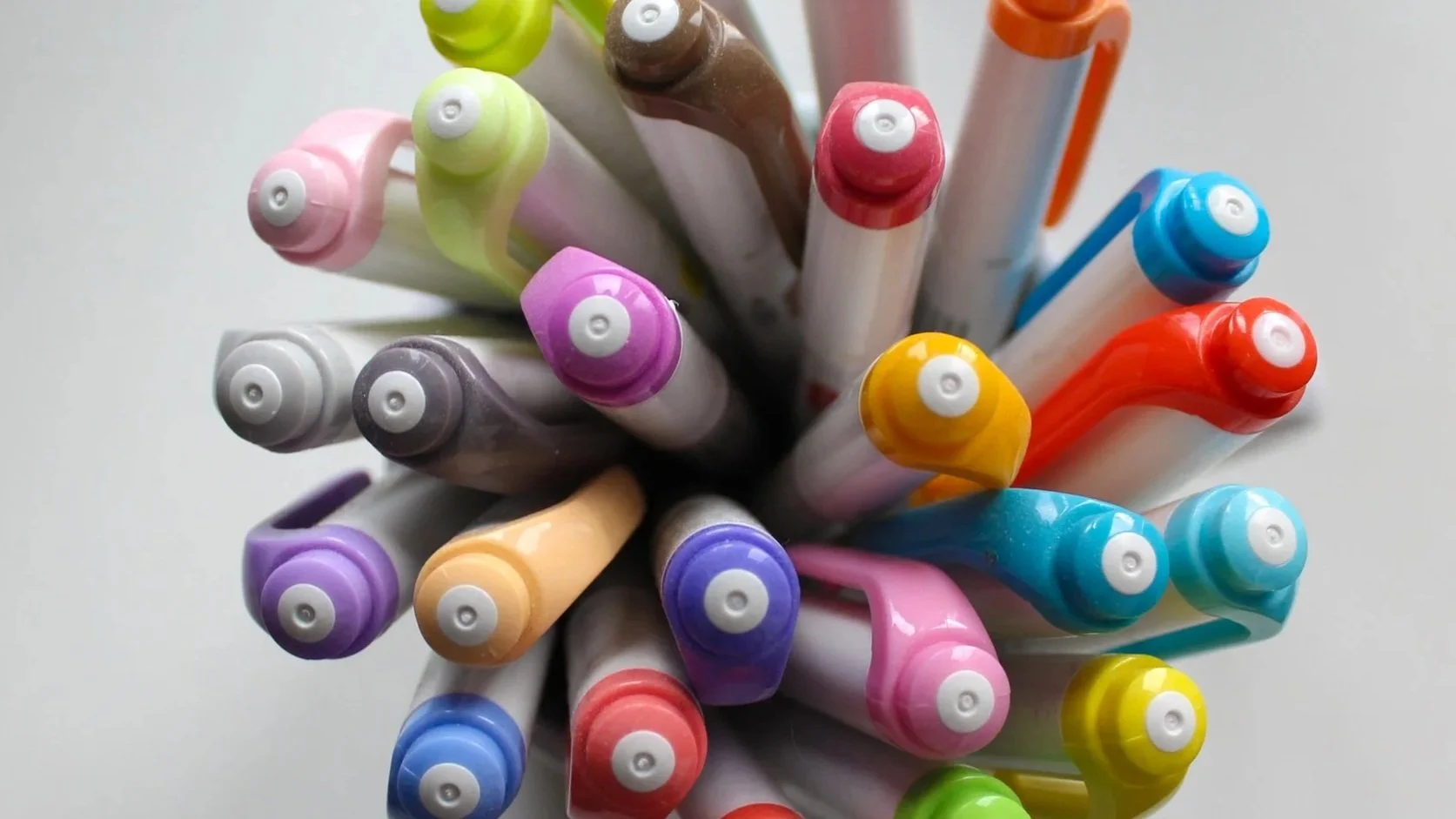 A top view of a collection of colorful felt-tip pens with their caps on, arranged in a circular pattern.
