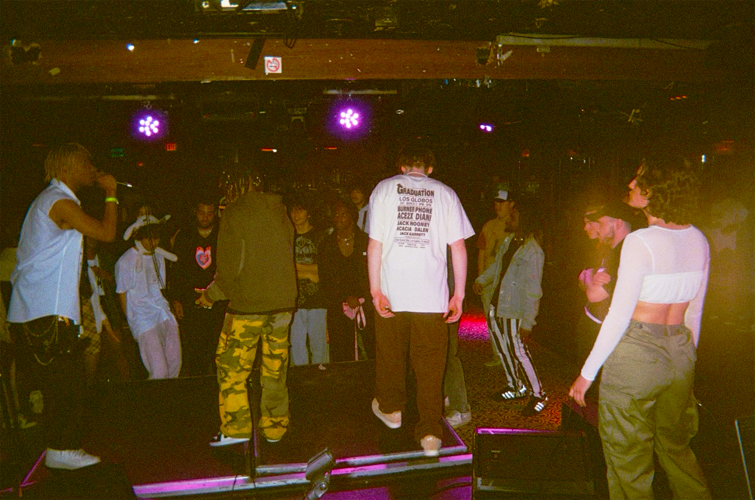 People dancing and socializing in a dimly lit nightclub with purple and pink lighting.