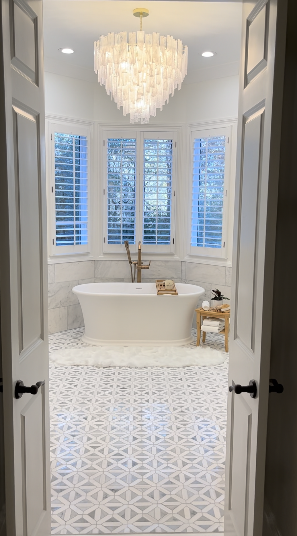Hill Home Construction, Atlanta, Georgia,. A bathroom with a white freestanding bathtub, a small wooden side table holding towels and plants, a soap tray, and a luxurious chandelier above.