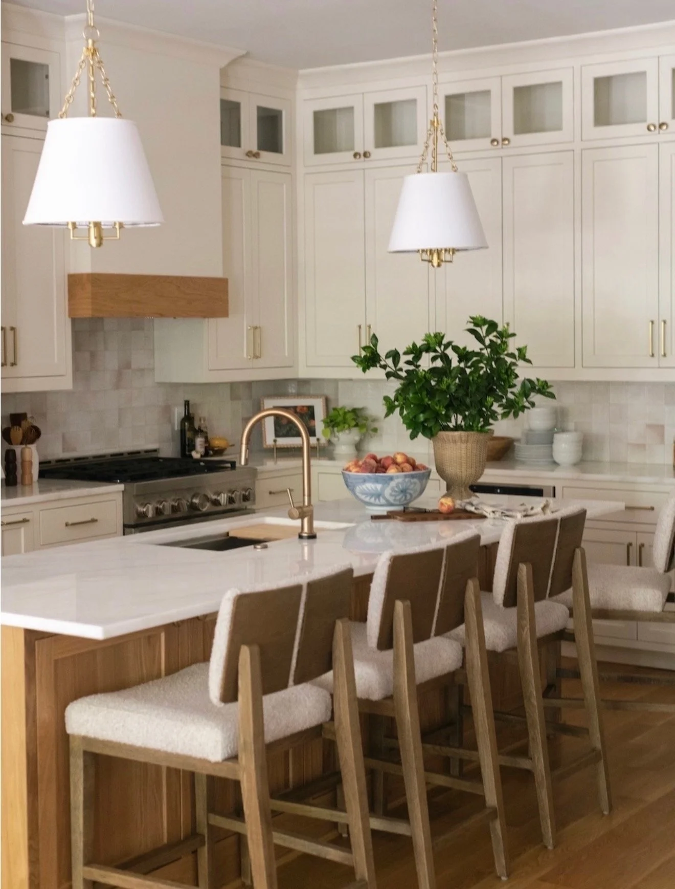 Hill Home Construction Finished Kitchen Remodel. A bright kitchen with white cabinets, a kitchen island with a wooden base, beige upholstered chairs, a bowl of vegetables, a large leafy green plant, hanging pendant lights. Atlanta, Georgia