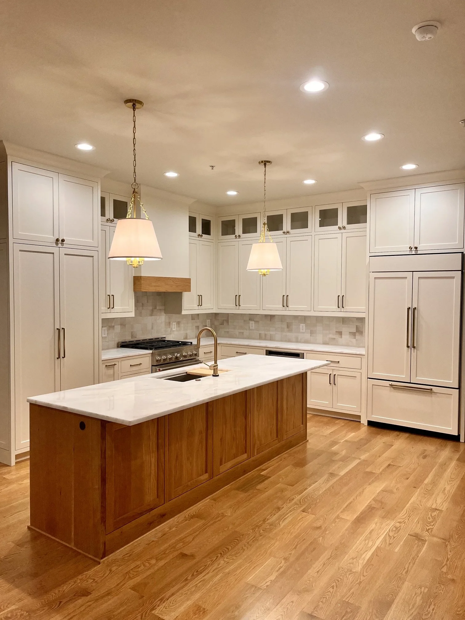 Modern kitchen with white cabinets, a kitchen island with a wooden base and white marble countertop, stainless steel appliances, hanging pendant lights, hardwood floors, and a tile backsplash.