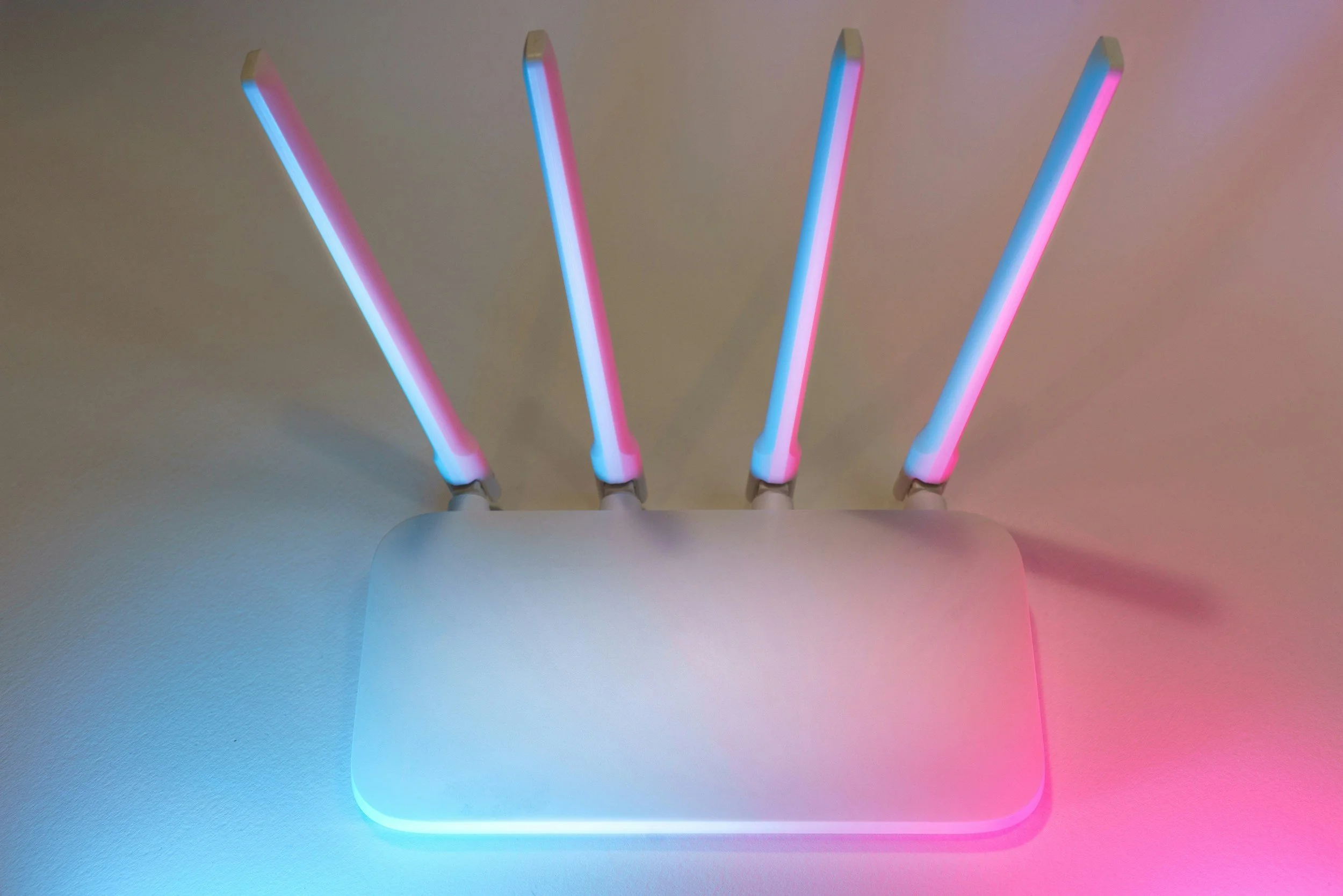A white router with four neon-colored LED light tubes emitting blue and pink colors, placed on a flat surface against a plain background.