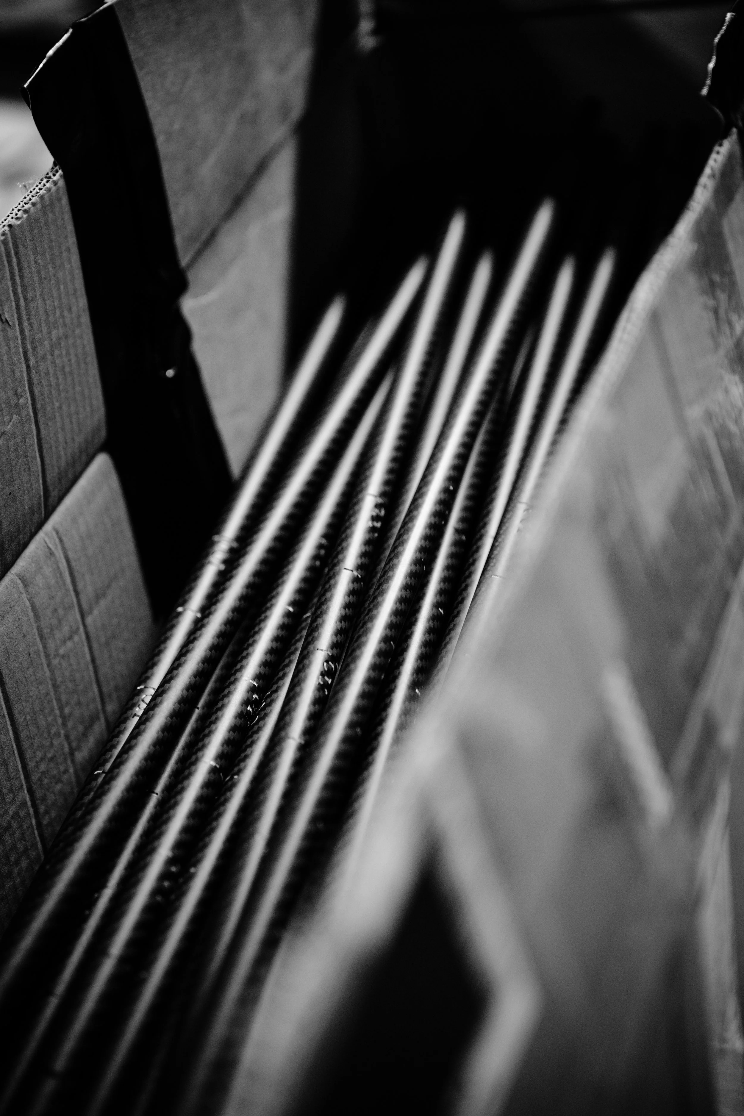 Close-up of black carbon fiber pipes or rods standing vertically in a cardboard box.
