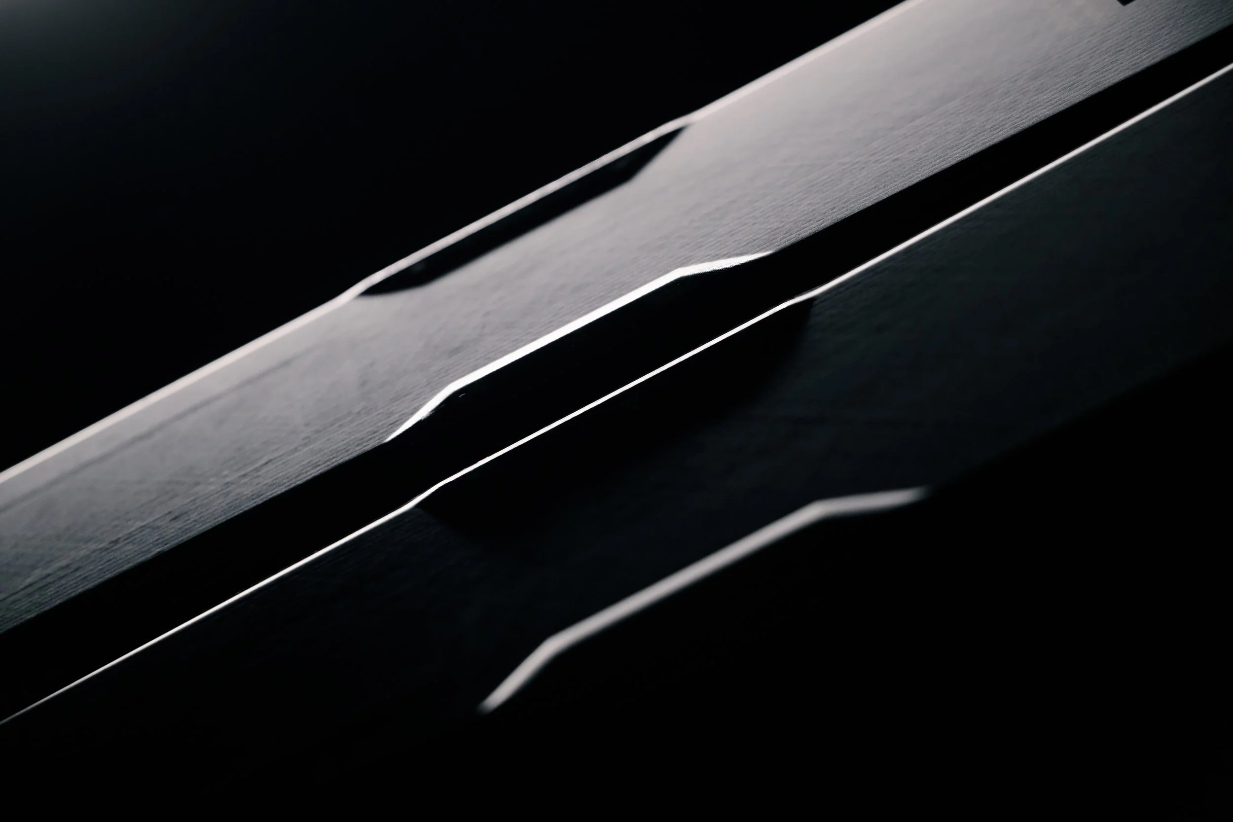 Close-up of a sleek, modern, black object with metallic accents and parallel lines, possibly part of an electronic device or machinery.