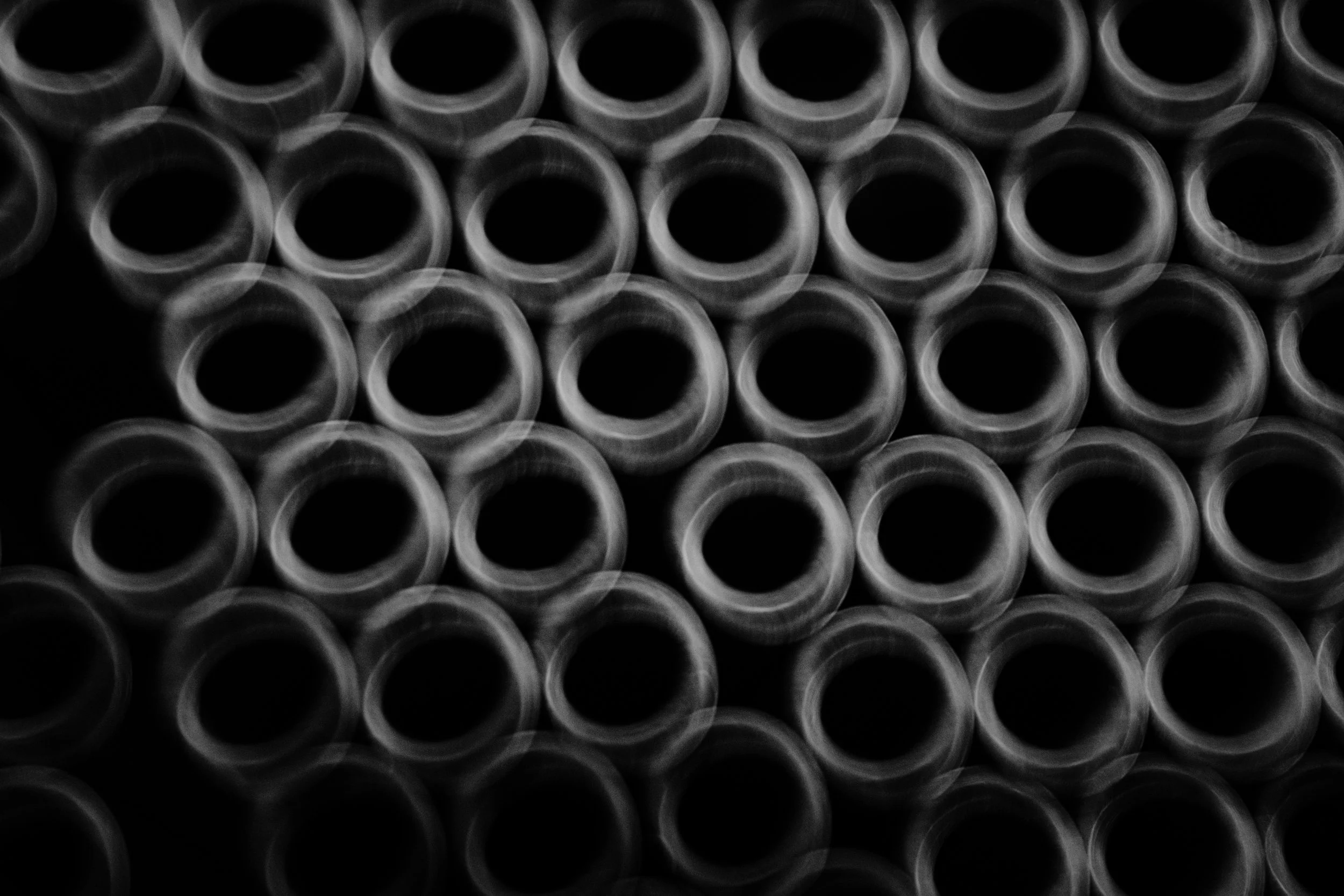 Close-up of multiple black cylindrical pipes arranged in a grid pattern, viewed from the front.