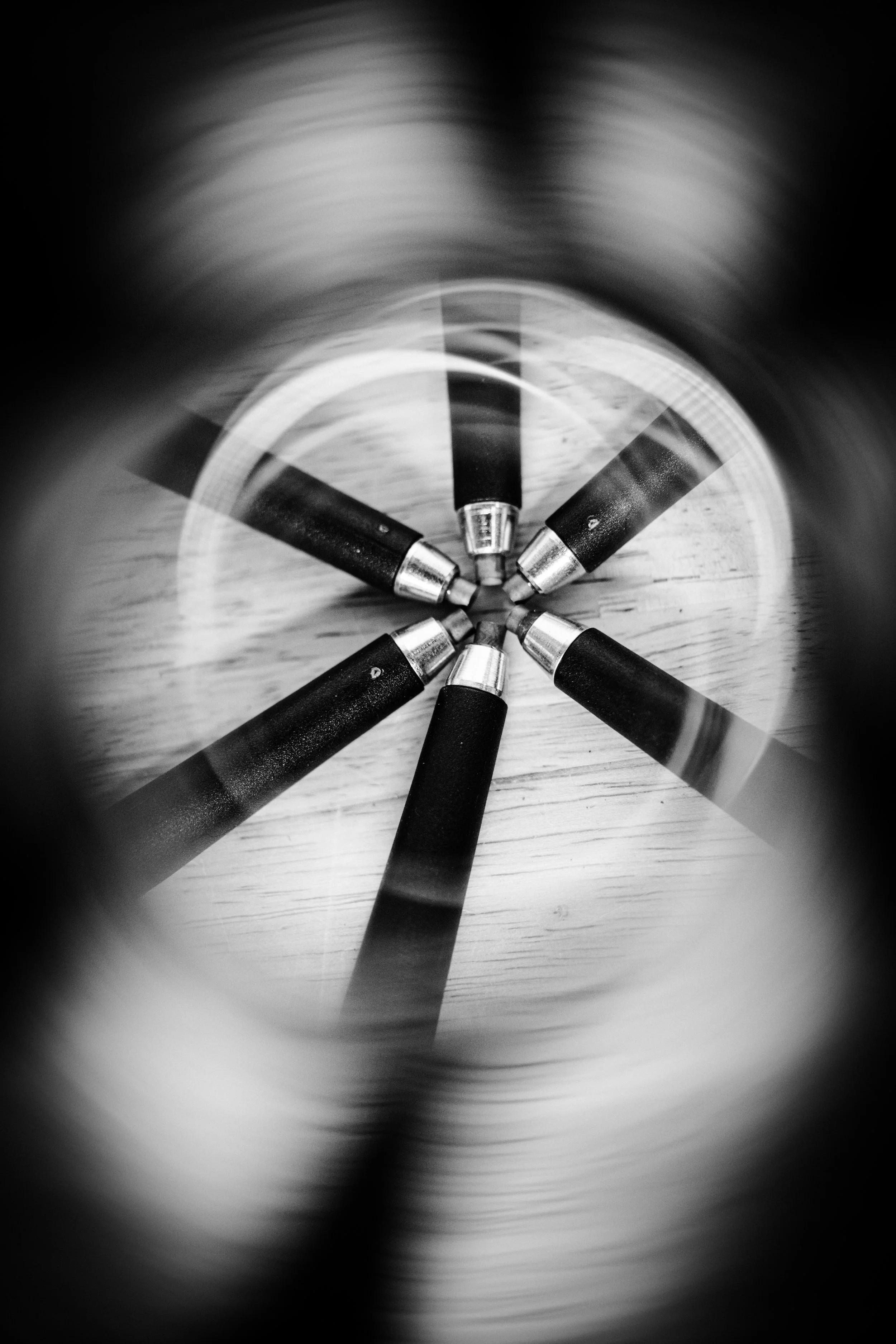Blurred black and white photo of five pens arranged in a circle on a wooden surface.