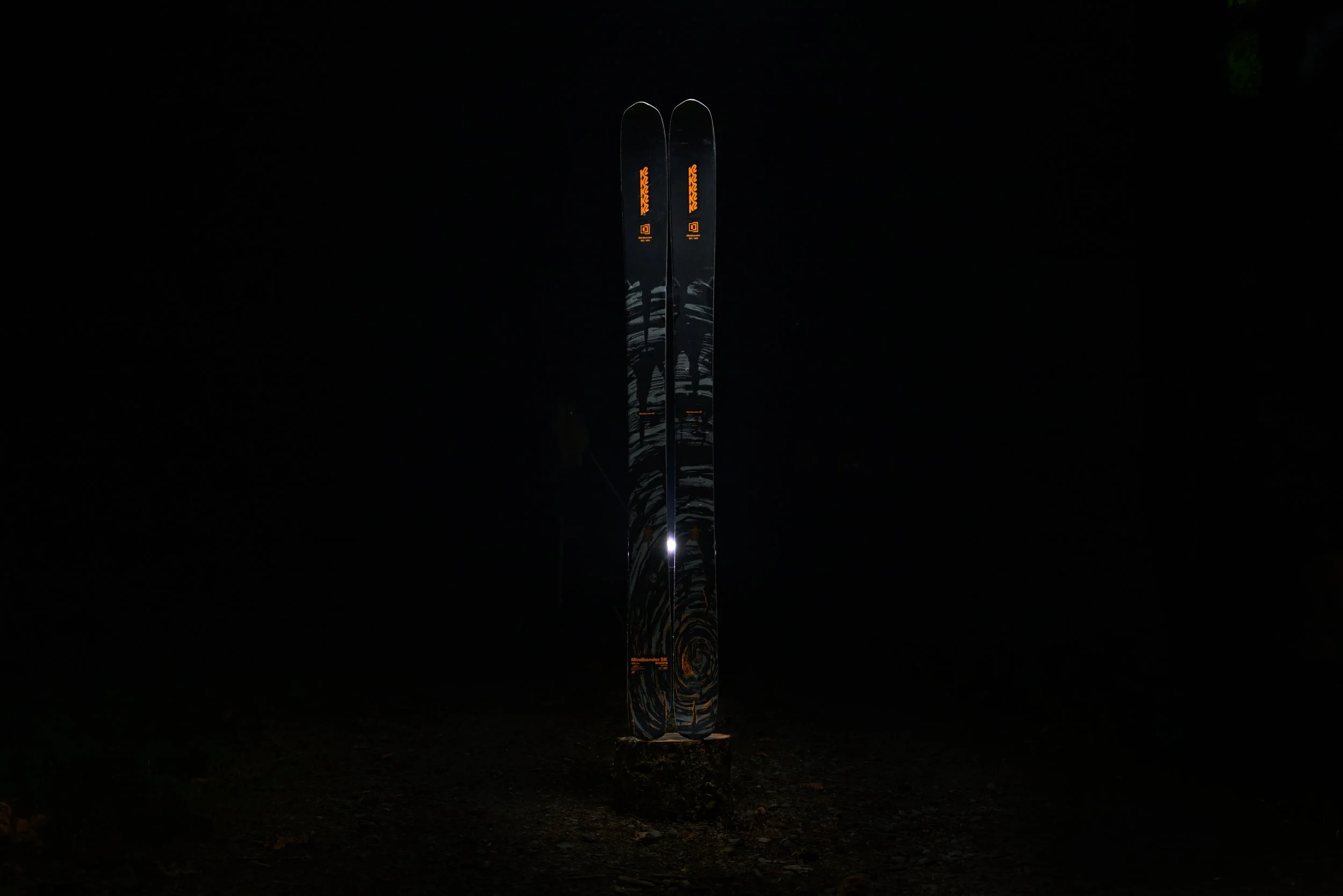 A pair of skis standing upright illuminated in the dark with orange and black designs.