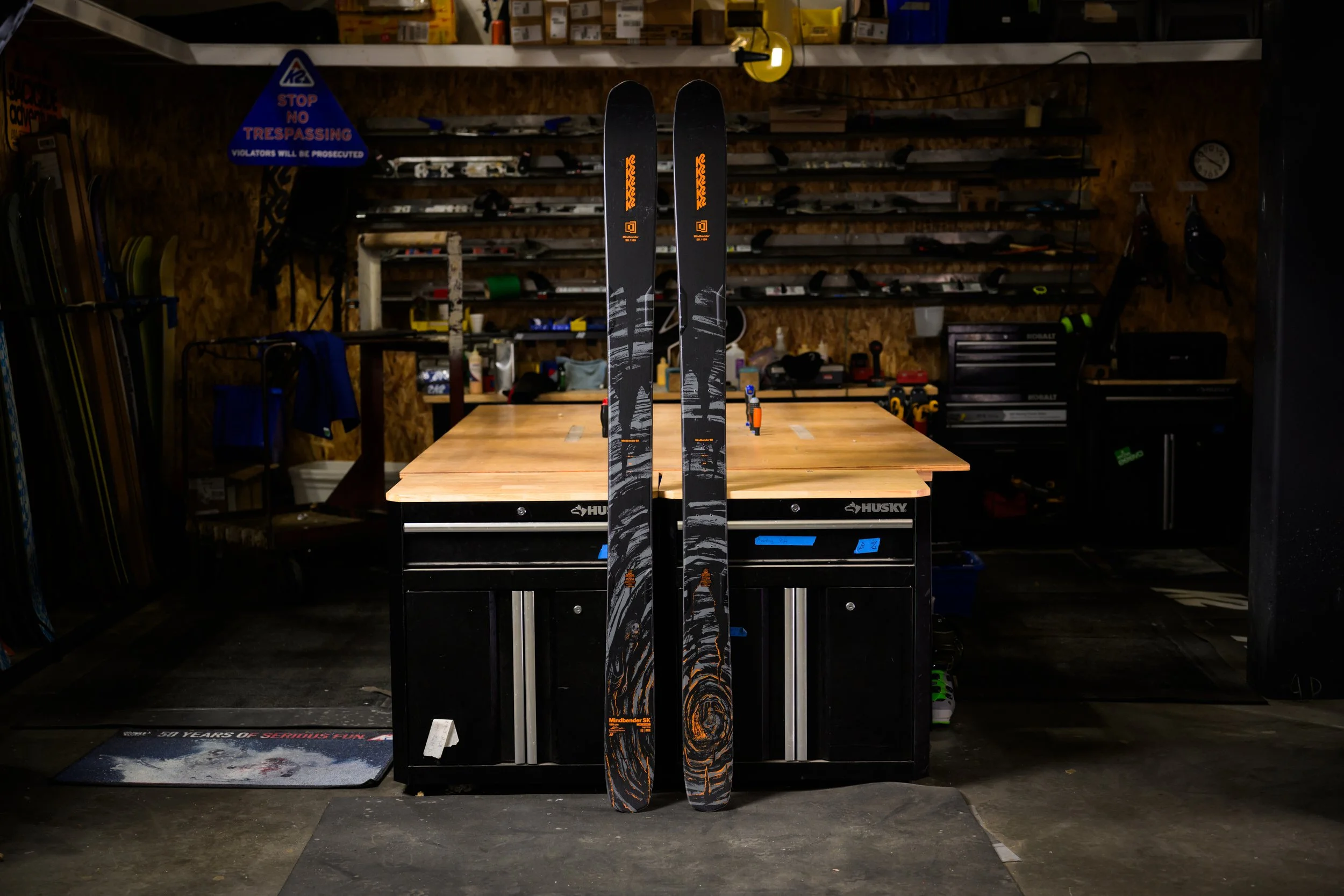 Pair of black skis with orange and white design standing upright in a workshop.