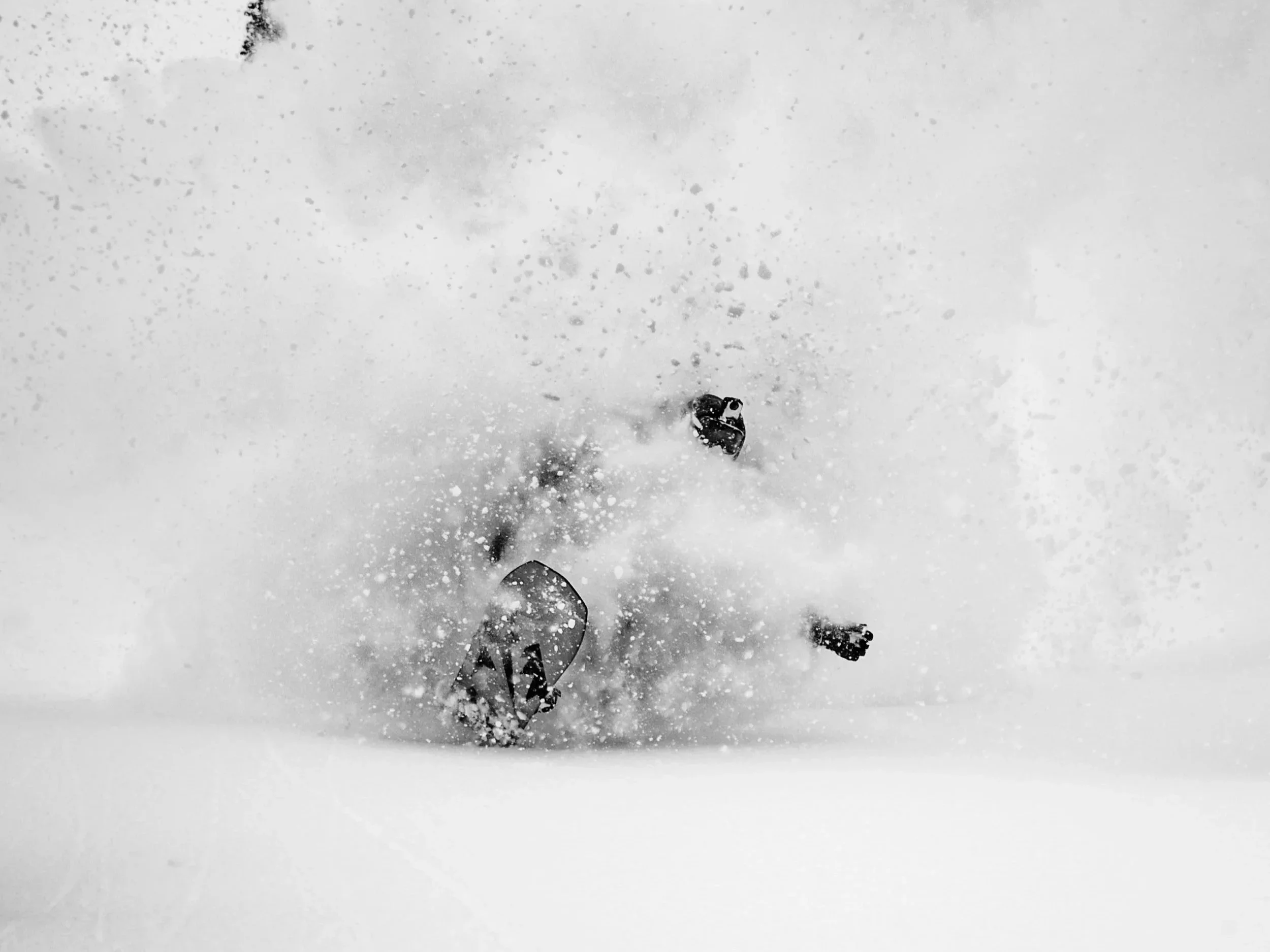 A snowboarder performing a trick on a snowy mountain slope, with snow spray around them and a mountainous landscape in the background.