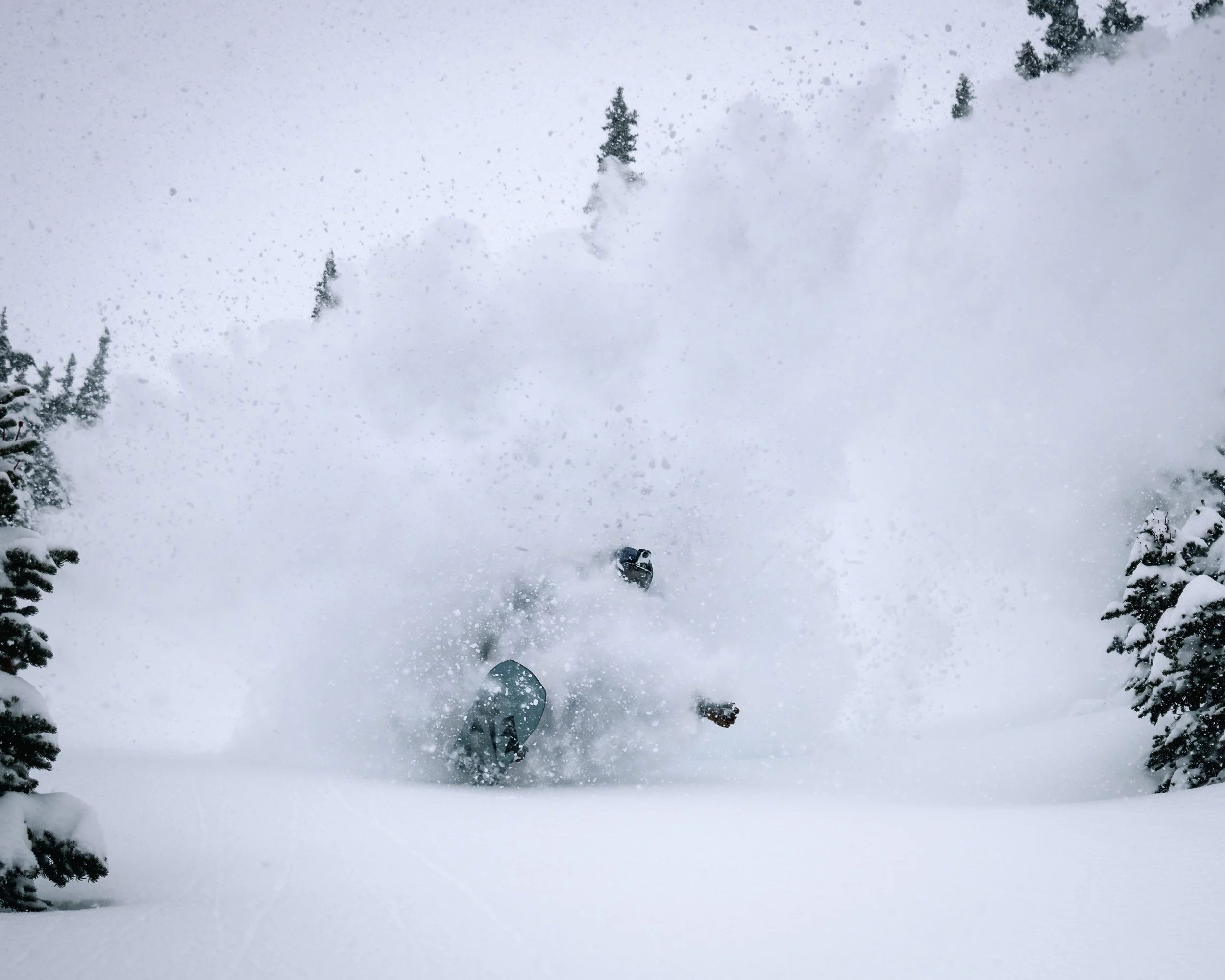 View from a skier or snowboarder looking down a snowy slope with trees on either side, snow falling heavily.