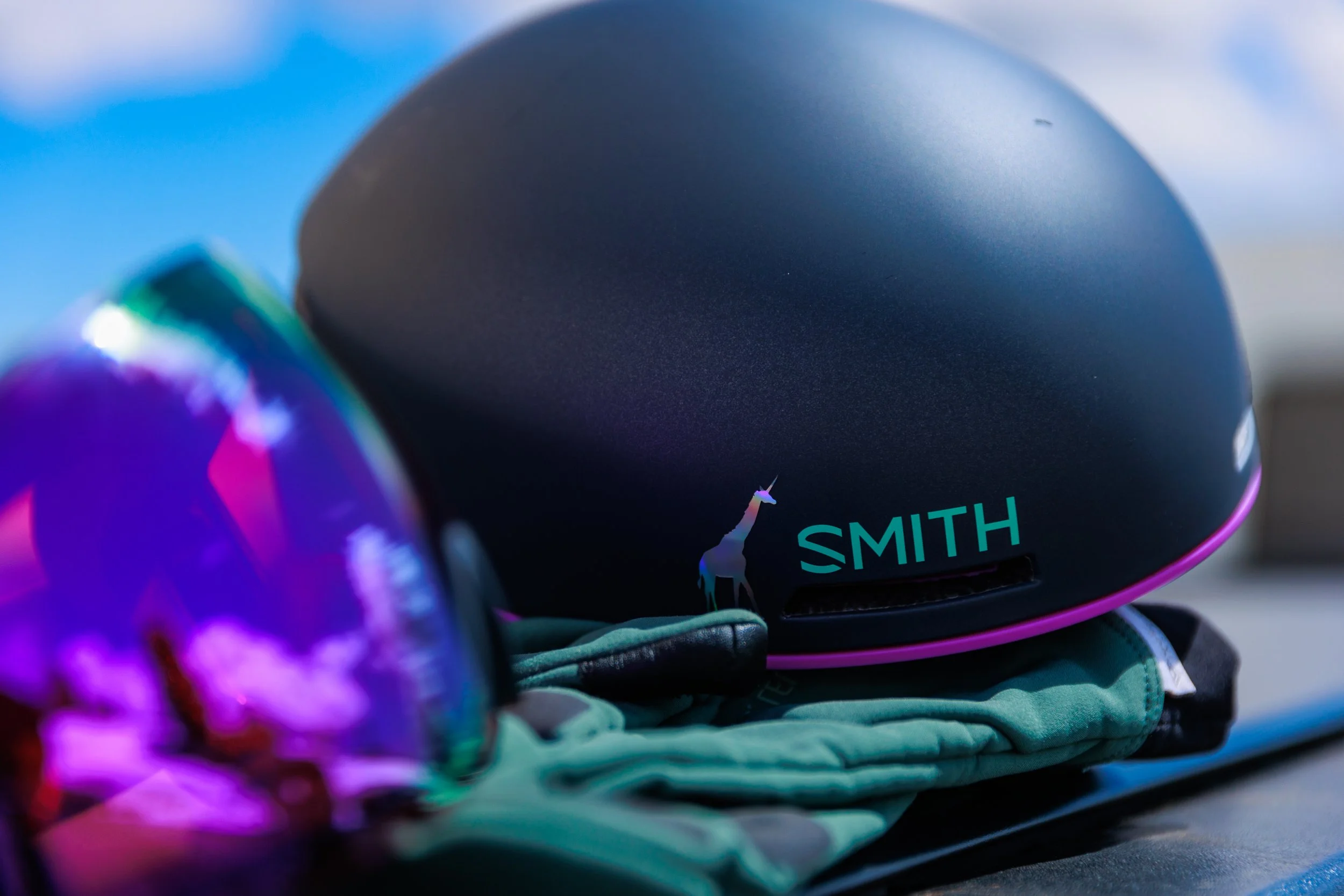 Close-up of a black tech gadget with the brand name 'SMITH' and a white unicorn logo, resting on folded colorful clothes with an iridescent reflective surface nearby.
