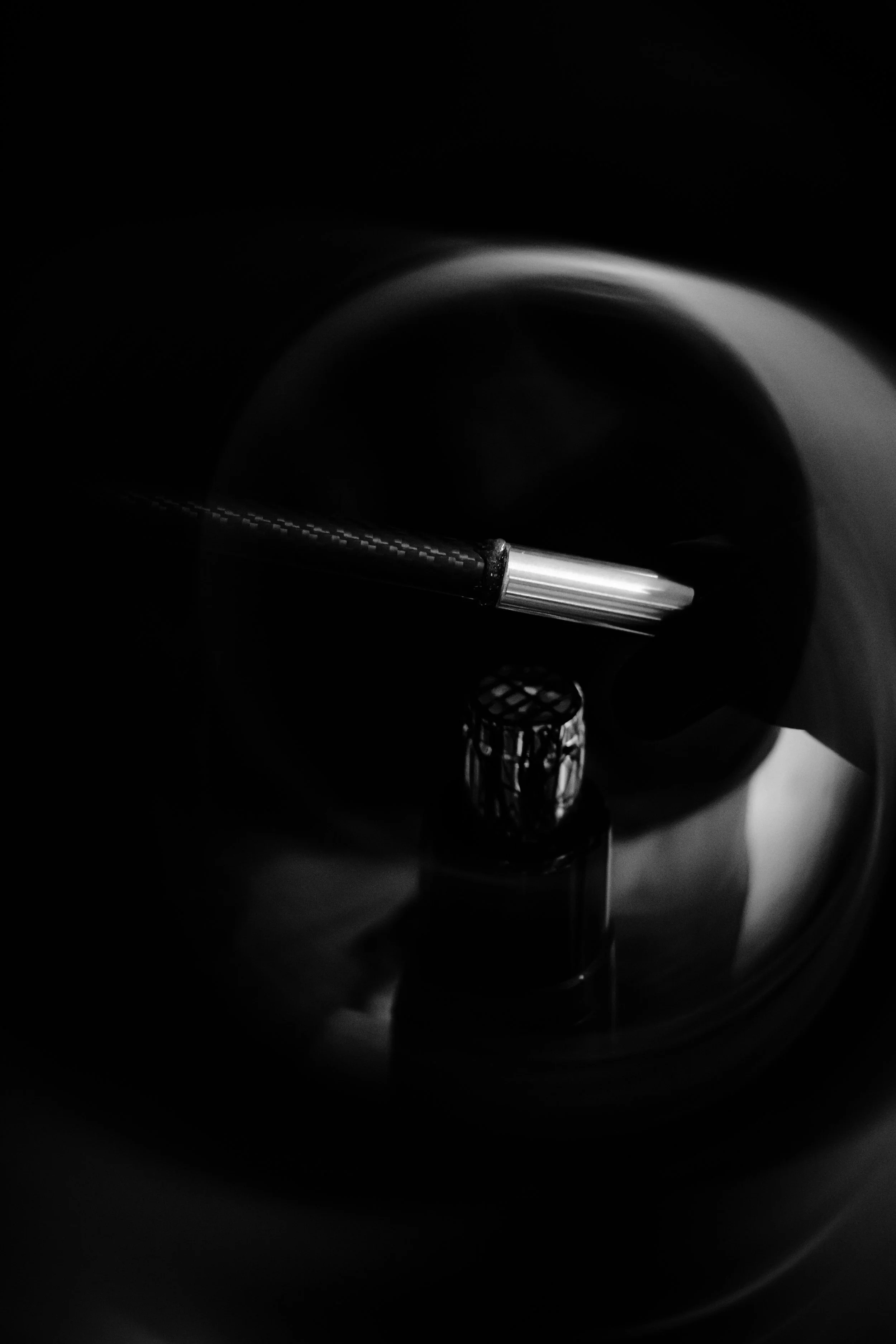 Close-up of a metallic fountain pen near a swirling dark liquid or ink in a circular container.