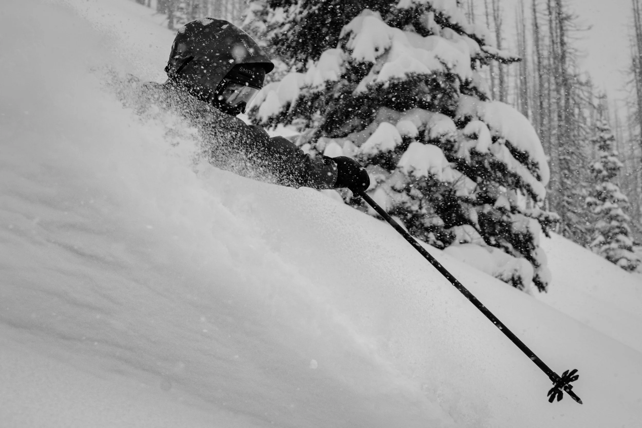 A person skiing in deep snow in a snowy forest with snow-covered trees in the background.