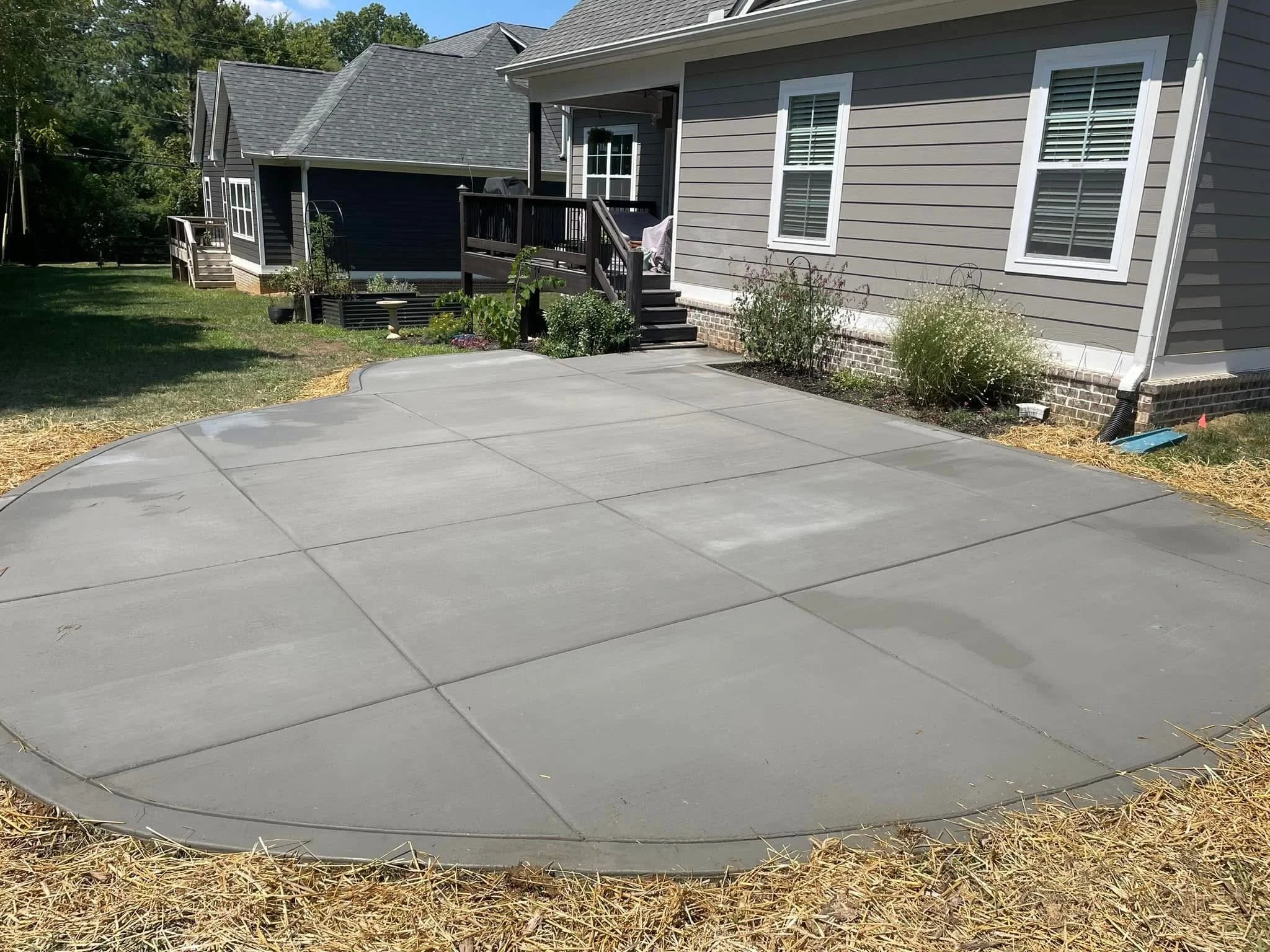 View of the backyard with a concrete patio, garden beds with plants, and a gray house with white trim and windows.