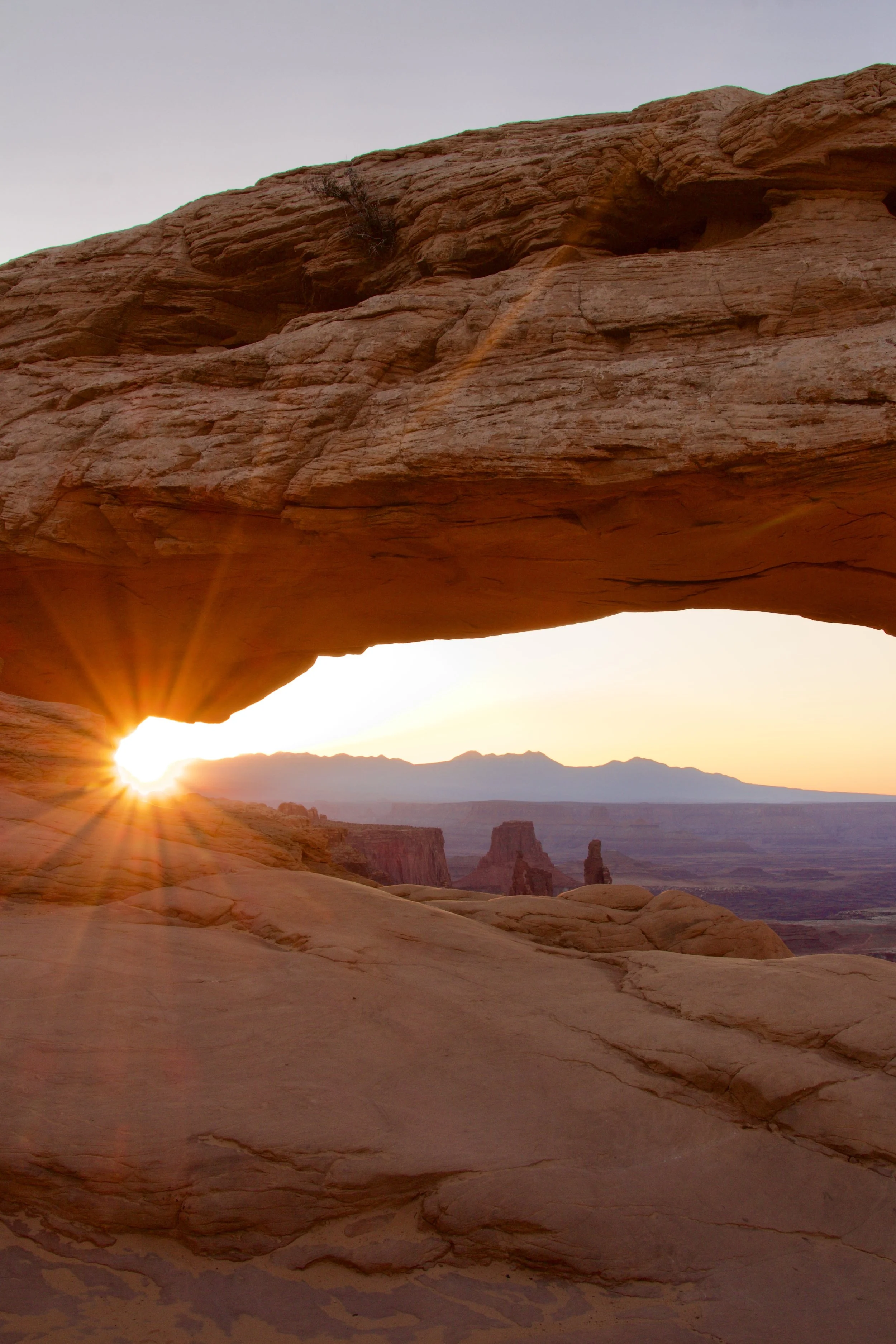 A natural rock formation with an arch-shaped opening set against a sunset sky in a desert landscape.