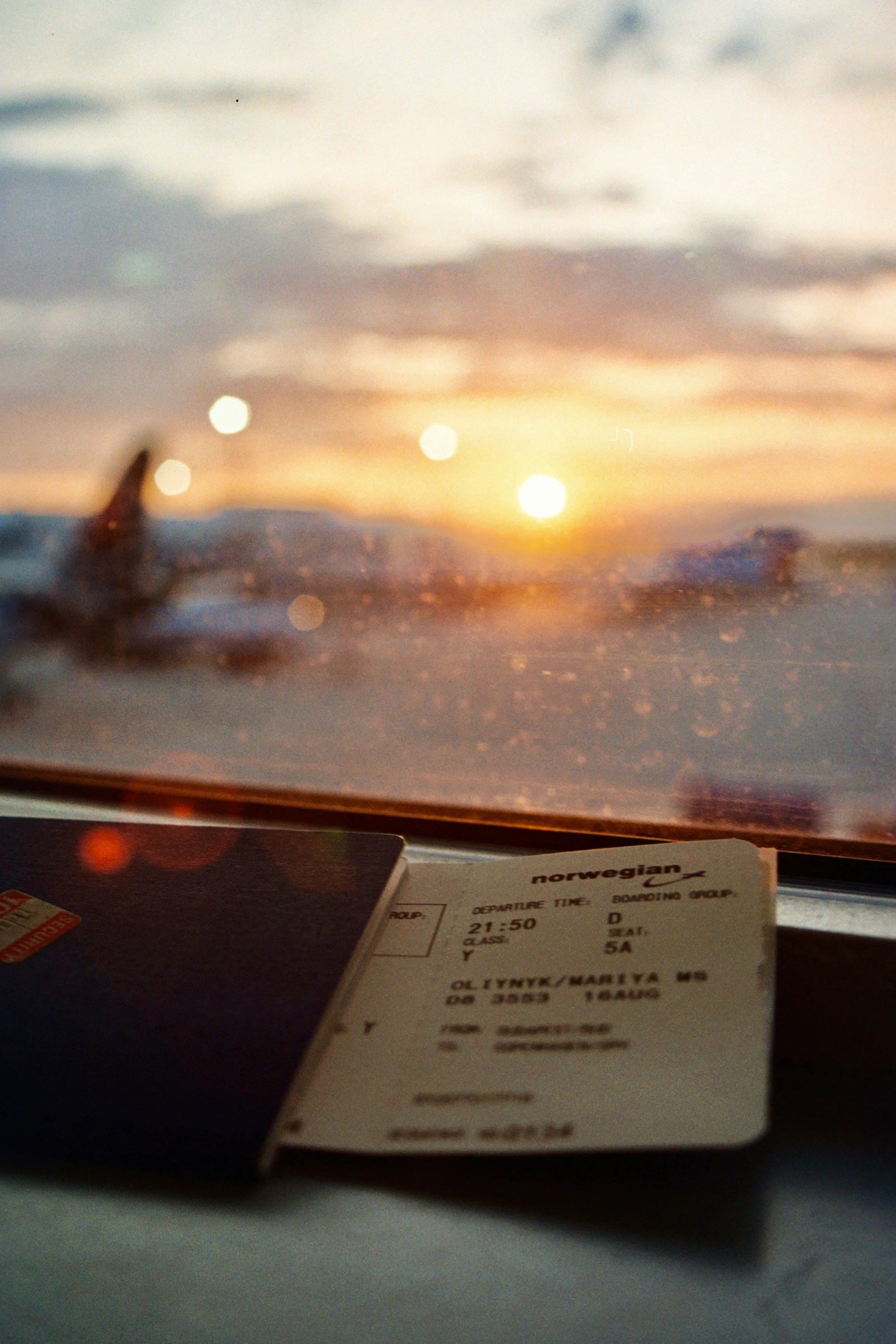 Airplane ticket on an airplane window ledge, with sunset sky visible through the window.