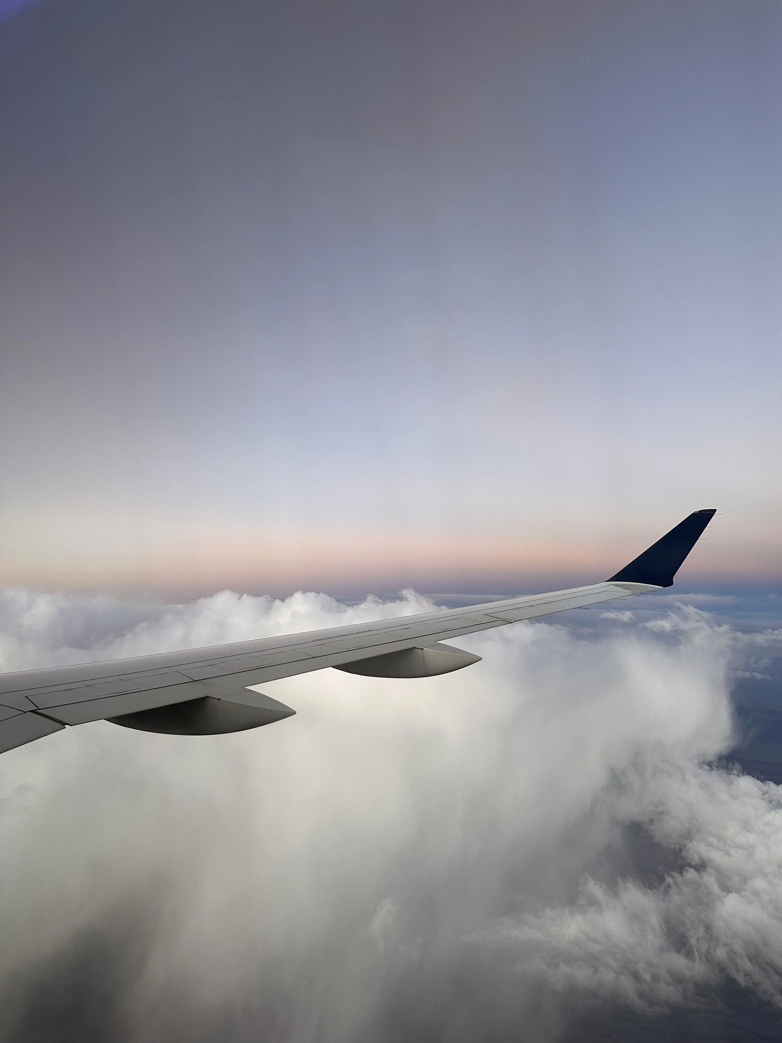View of an airplane wing flying above clouds during sunset or sunrise with a colorful sky.