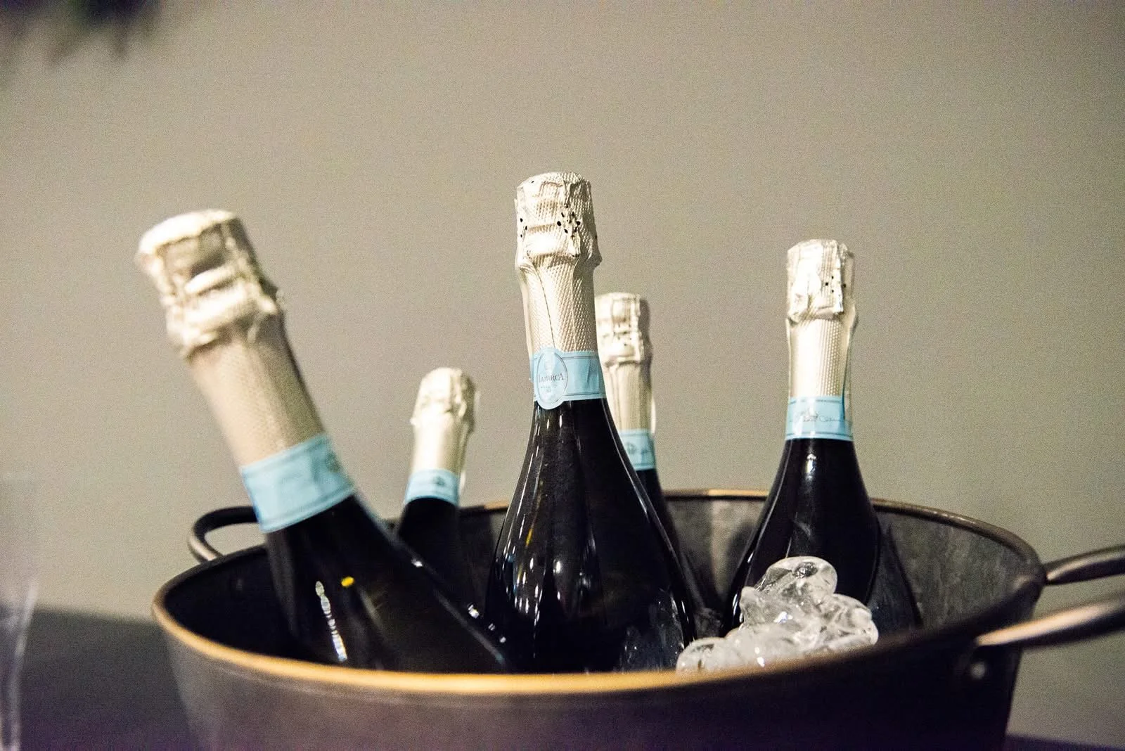 Several bottles of champagne chilling in a black ice bucket filled with ice cubes.