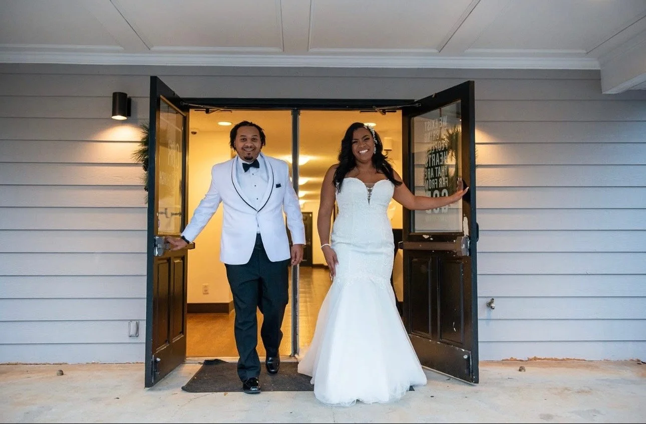 A bride and groom standing outside and smiling on their wedding day.