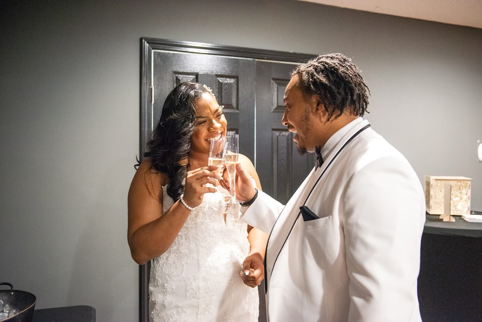 A bride and groom toasting with champagne glasses. The bride is wearing a white wedding dress and the groom is dressed in a white tuxedo.