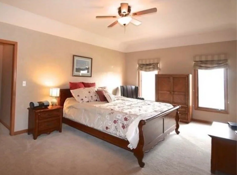 A bedroom with a wooden bed, floral bedding, two nightstands with lamps, a wooden dresser, and two windows with beige valances.