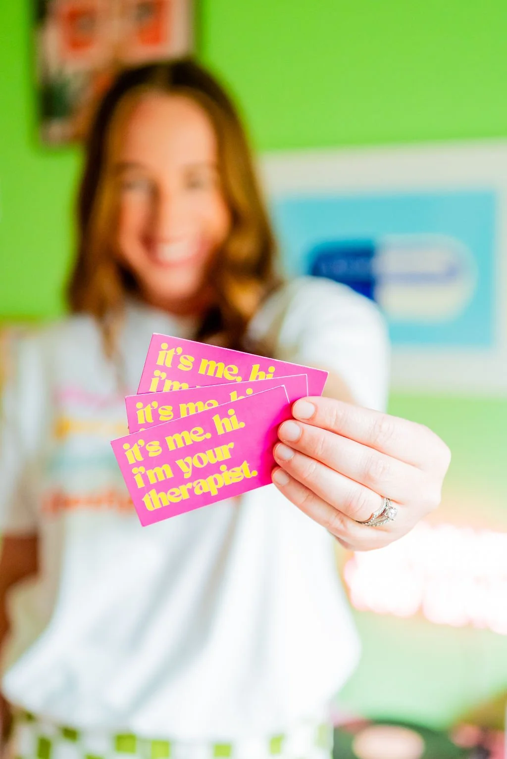 Texas anxiety therapist wearing a "Therapy Is Cool" shirt while holding branded business cards, promoting virtual therapy for anxiety, life transitions, and personal growth.