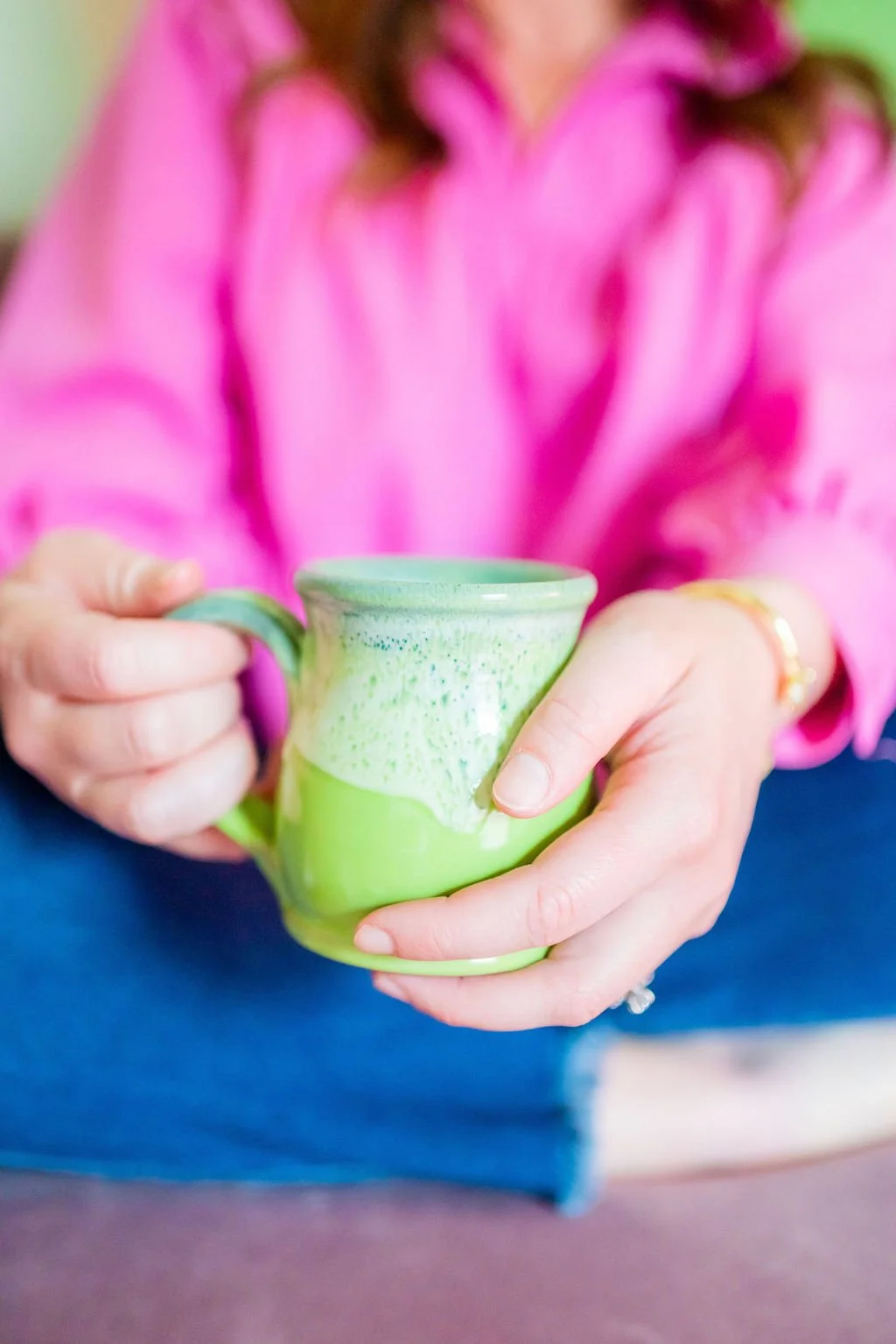 Green coffee mug in the foreground with a therapist blurred in the background, representing online therapy and telehealth counseling for adults across Texas.