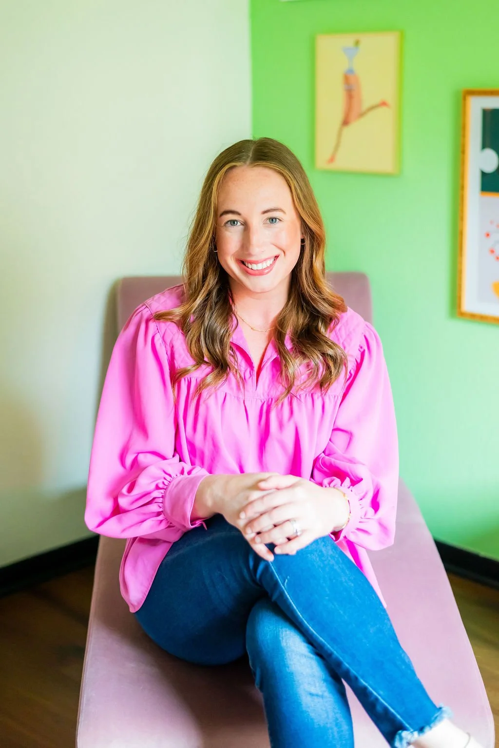 Mental health therapist in Texas sitting in a pink chair surrounded by colorful artwork and a disco ball, creating a welcoming space for virtual counseling and telehealth therapy.