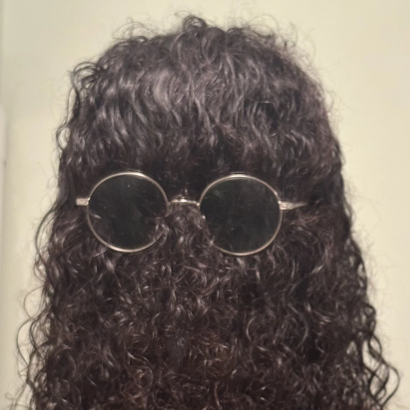 Person with long, curly dark hair wearing round, black glasses over his hair like Cousin Itt.