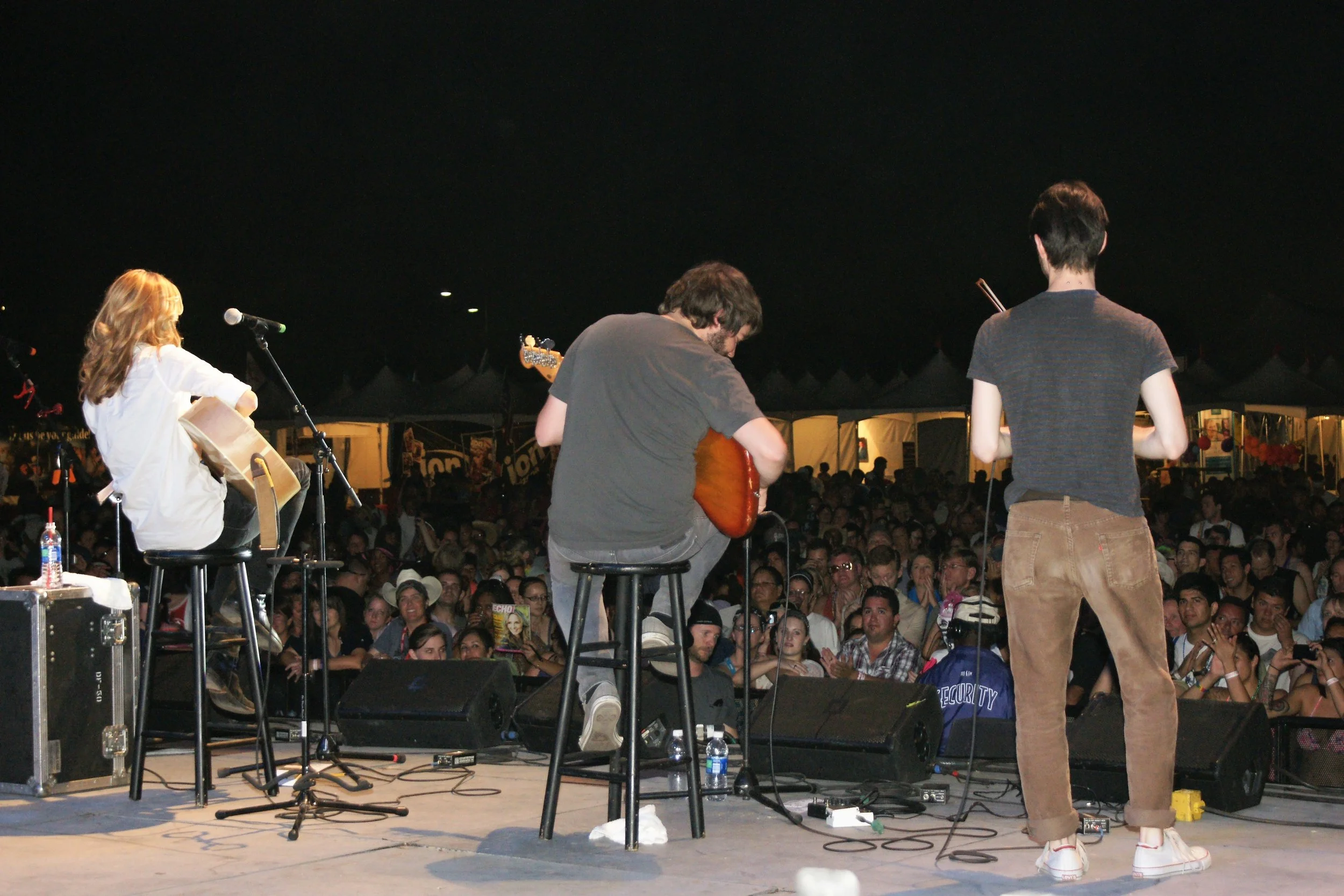 Musicians performing on stage at night with a large audience in front.