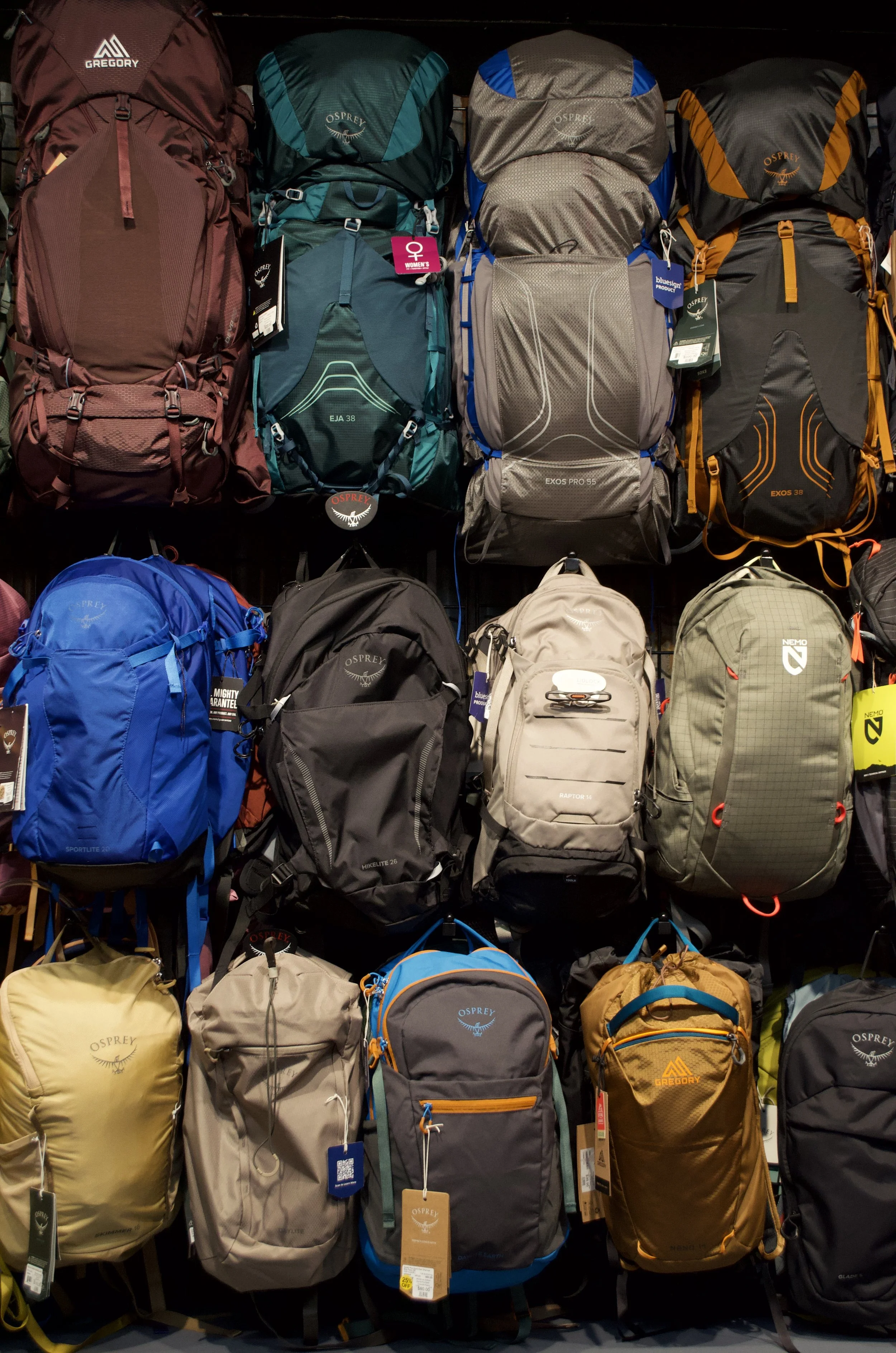 Display of various Osprey hiking backpacks in different colors and sizes on a store wall.