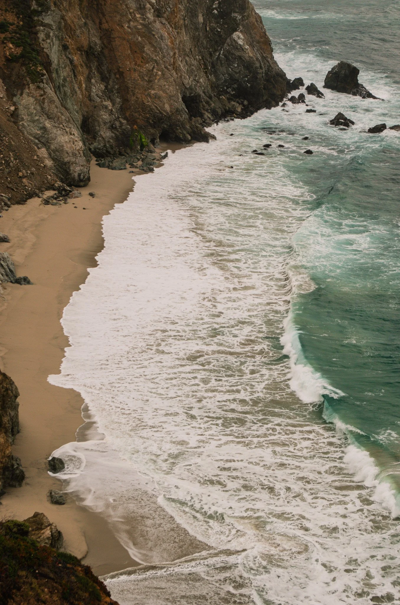 Coastal scene with cliffs, sandy beach, rocks, and ocean waves.