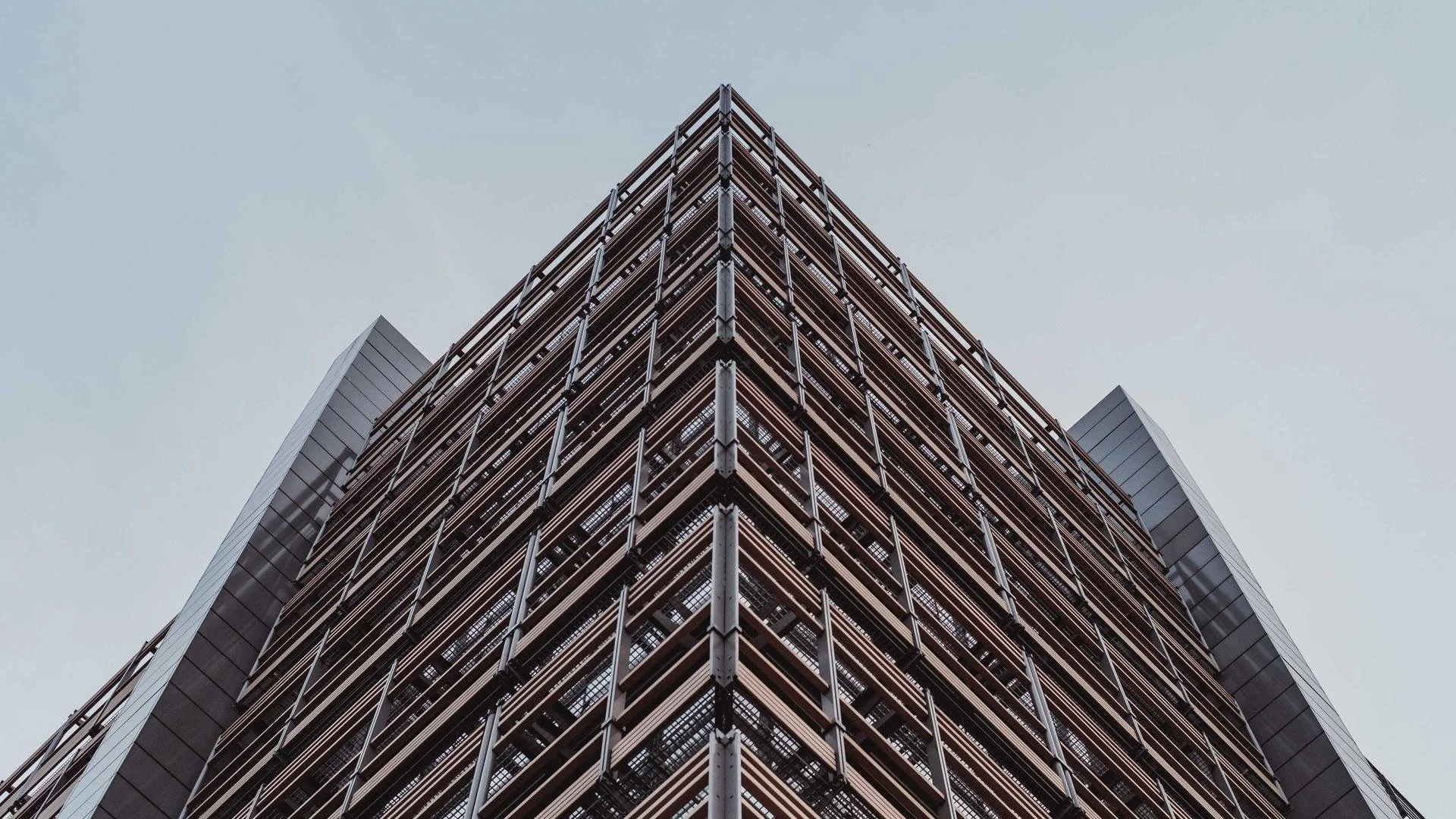 Low-angle view of a modern glass skyscraper building with symmetrical architecture, metal and glass facade, against an overcast sky.