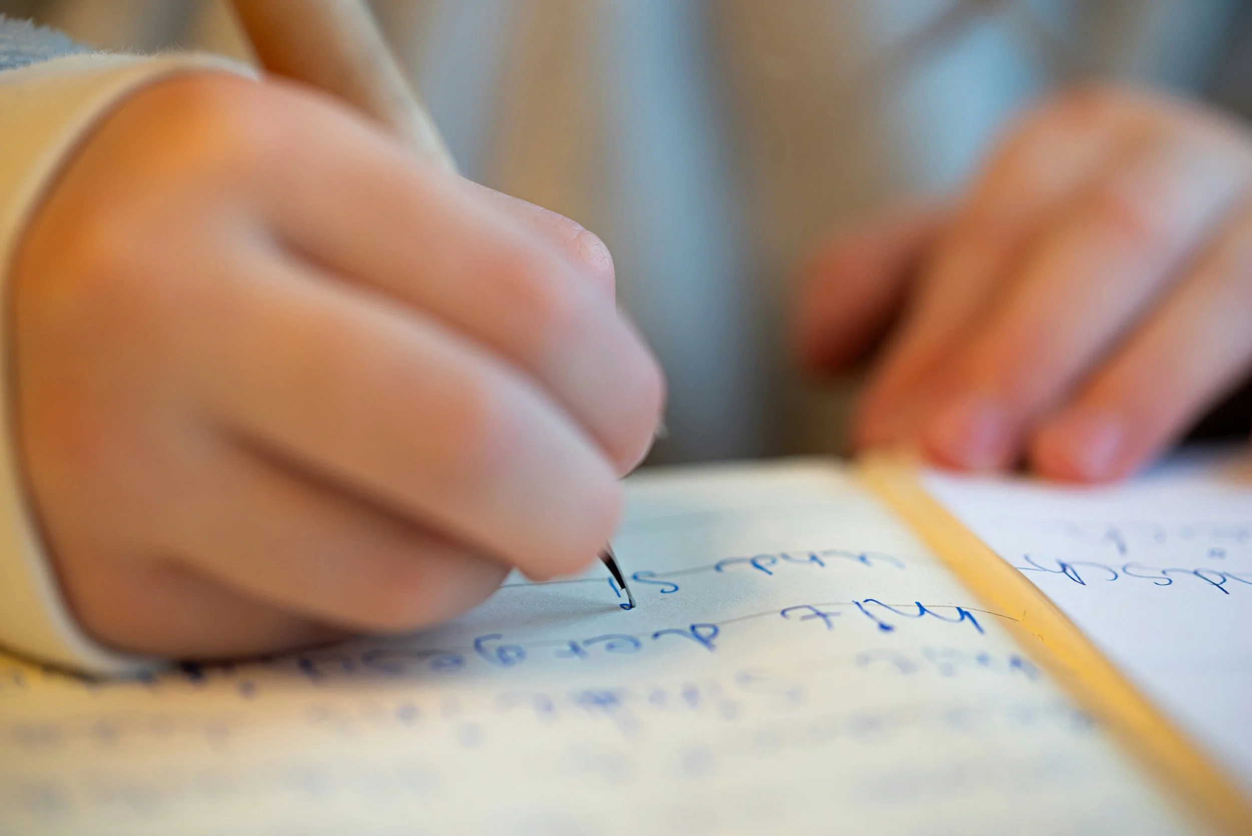 Close-up of a person's hand writing with a pen on a notebook with handwritten notes.