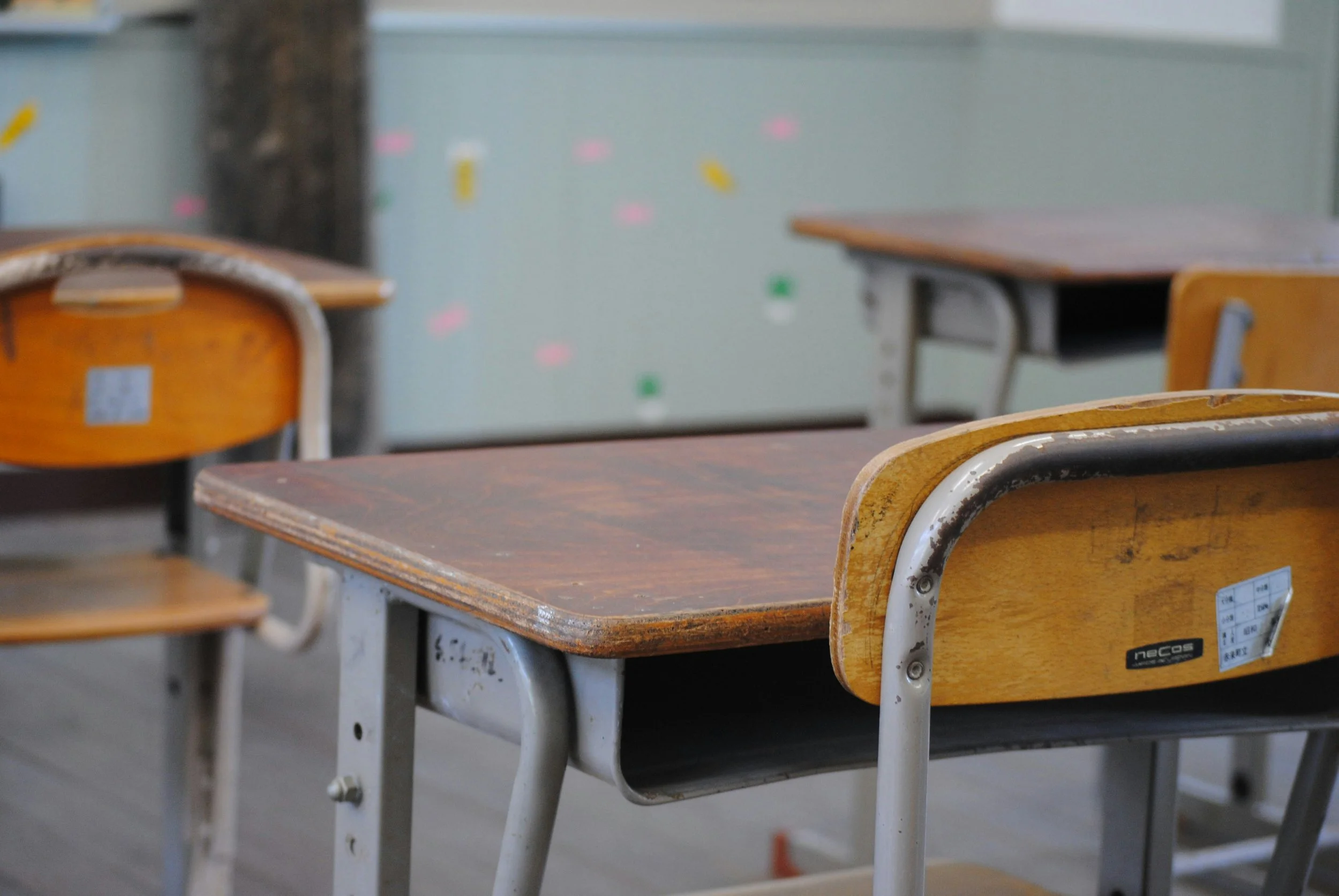 Empty wooden desks with metal frames in an empty classroom.