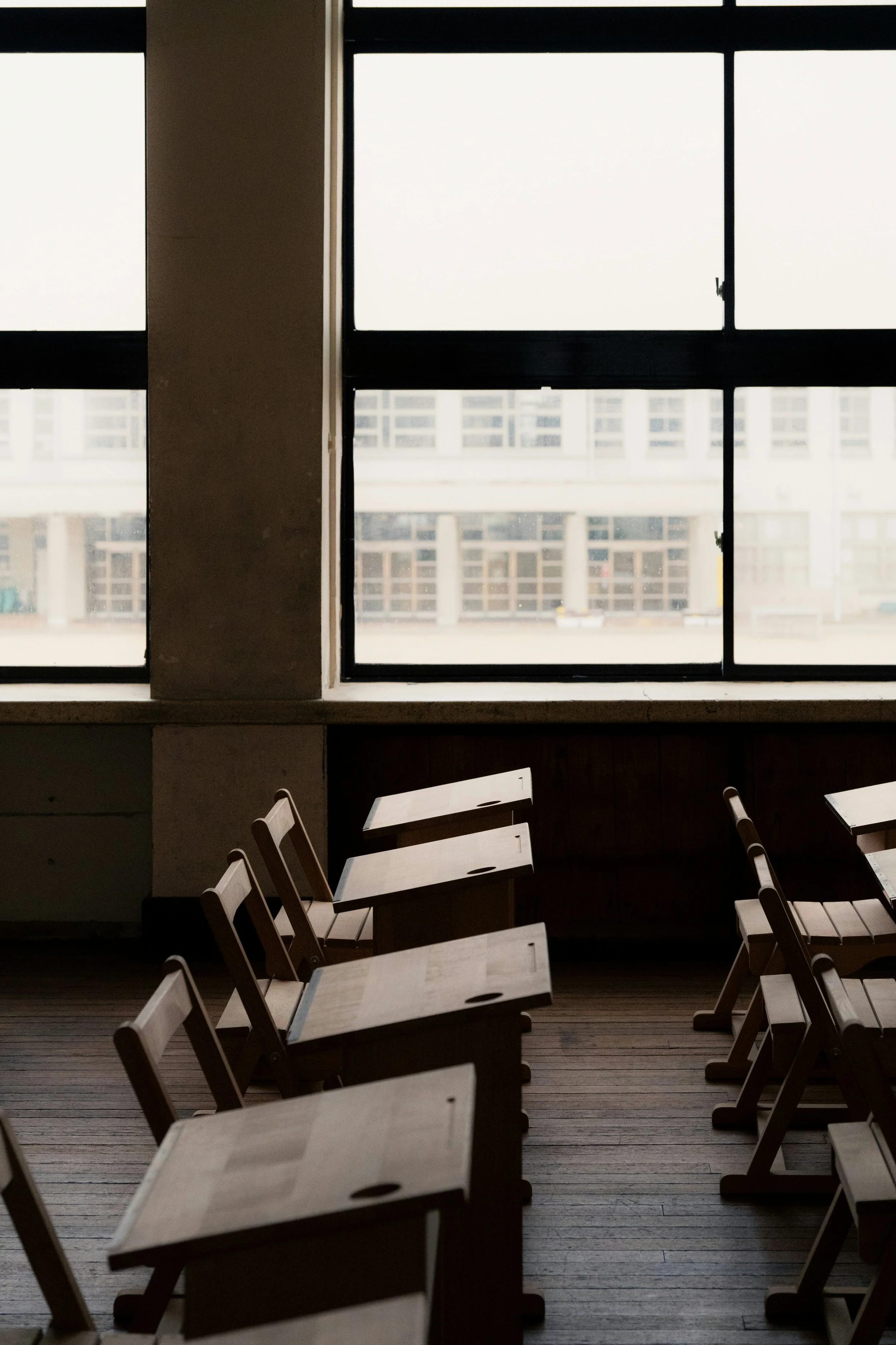 Empty chairs and tables inside a room with large windows showing a view of a building outside.