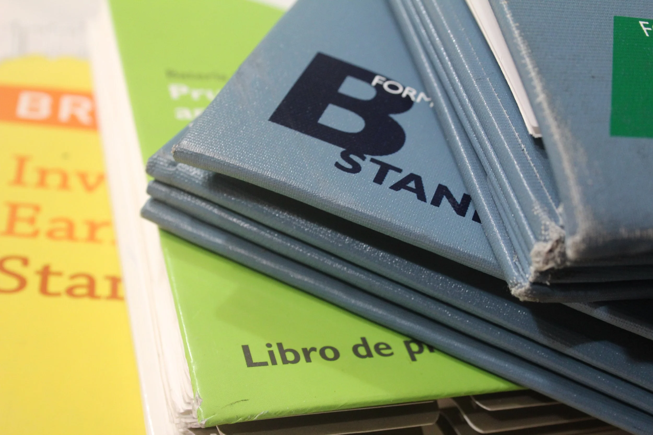 Close-up of a blue book with the title 'B' and 'for' visible on the cover, stacked on other colorful books with partially visible titles, including yellow and green covers, on a bookshelf.