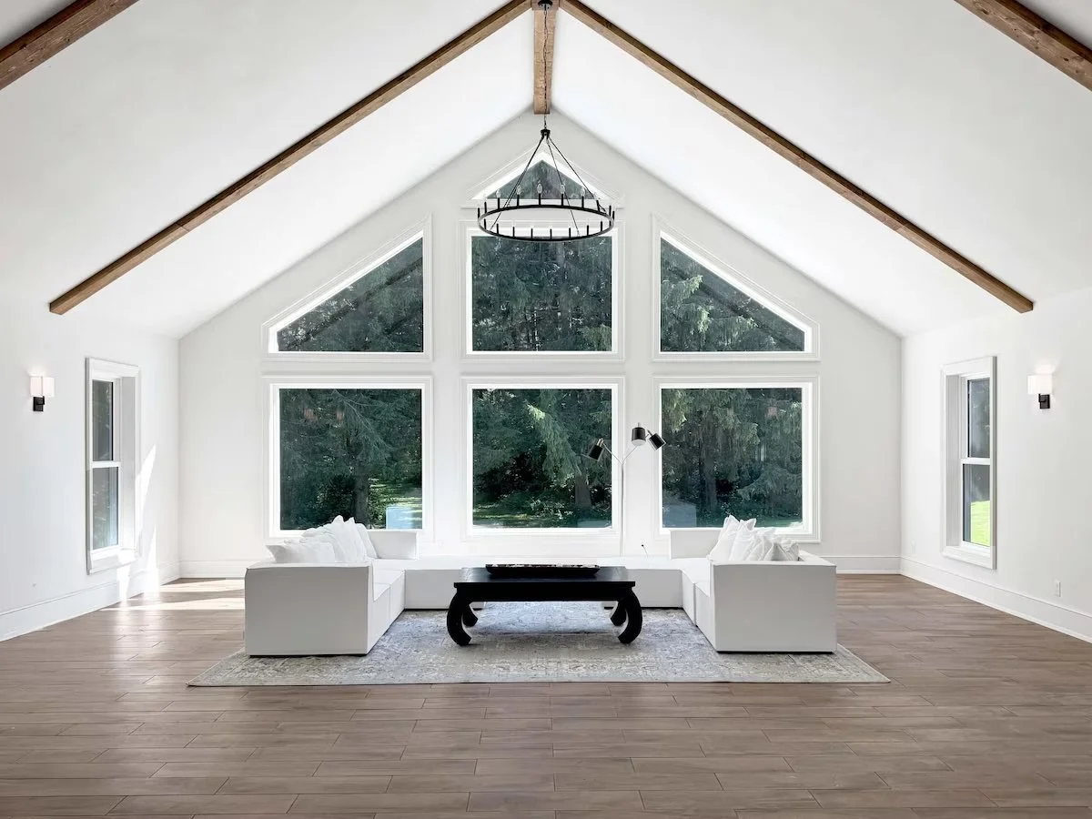 Bright living room with large triangular windows, white sofas, a black coffee table, and a modern chandelier.