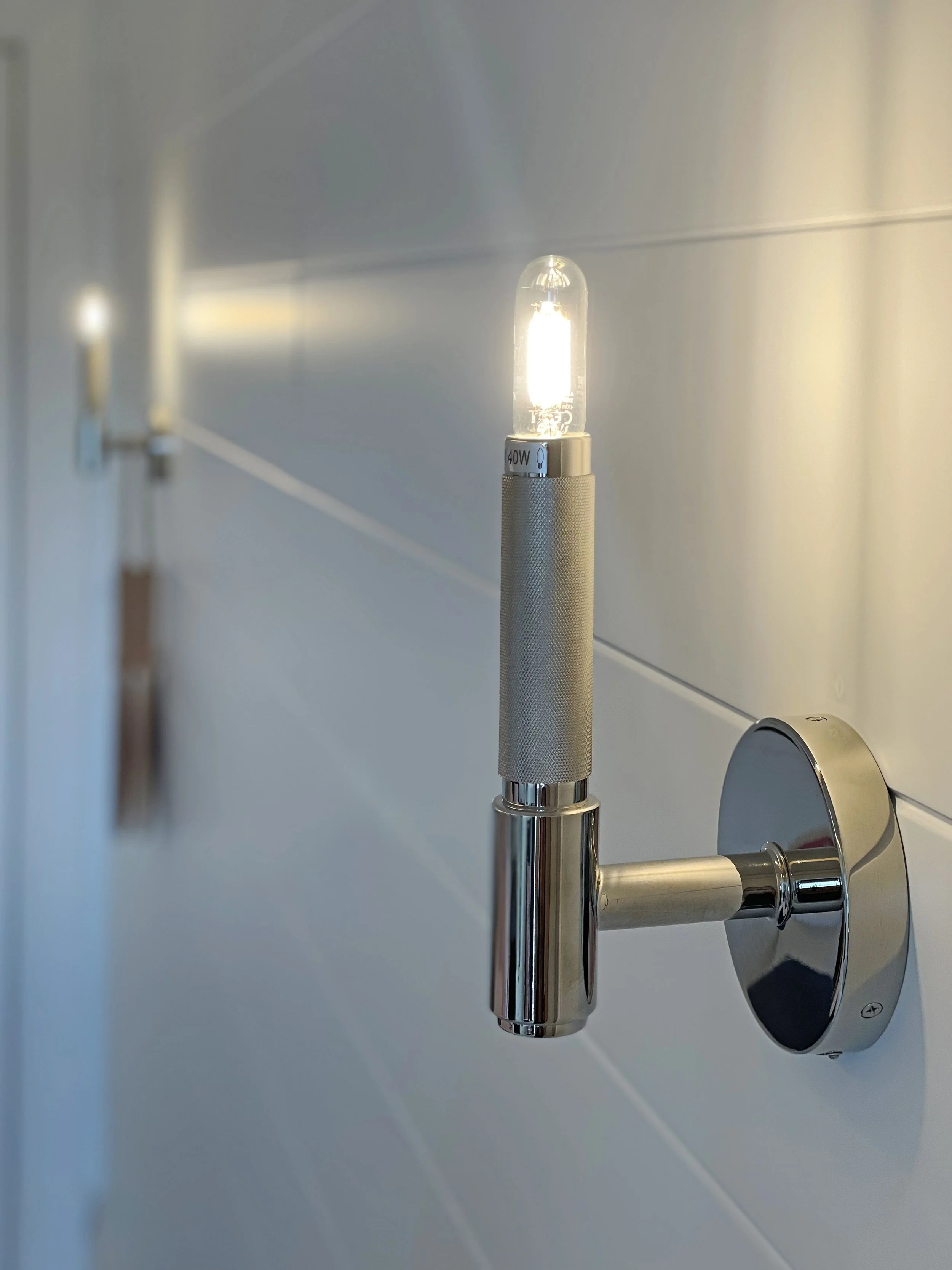 L'immagine mostra un applique a muro da 40 watt installato sopra un pannello di boiserie bianca.