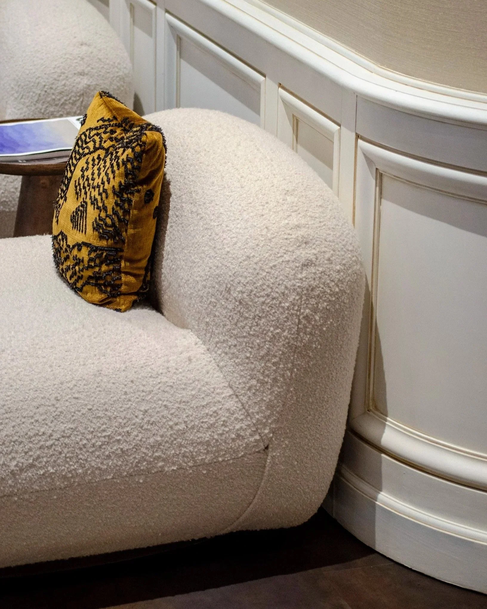 Morbida poltrona beige con cuscino giallo con motivi neri, parte di un arredamento di stanza con mobile bianco e pavimento in legno