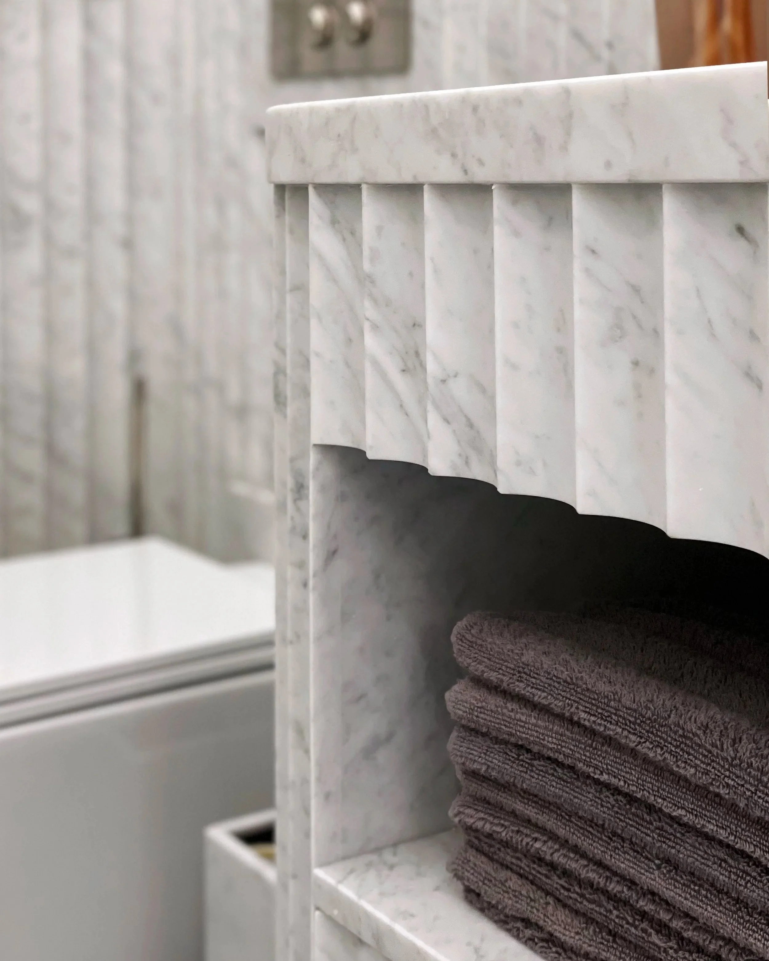 Particolare di un bagno con panni in tessuto grigio arrotolati su mensola di marmo.