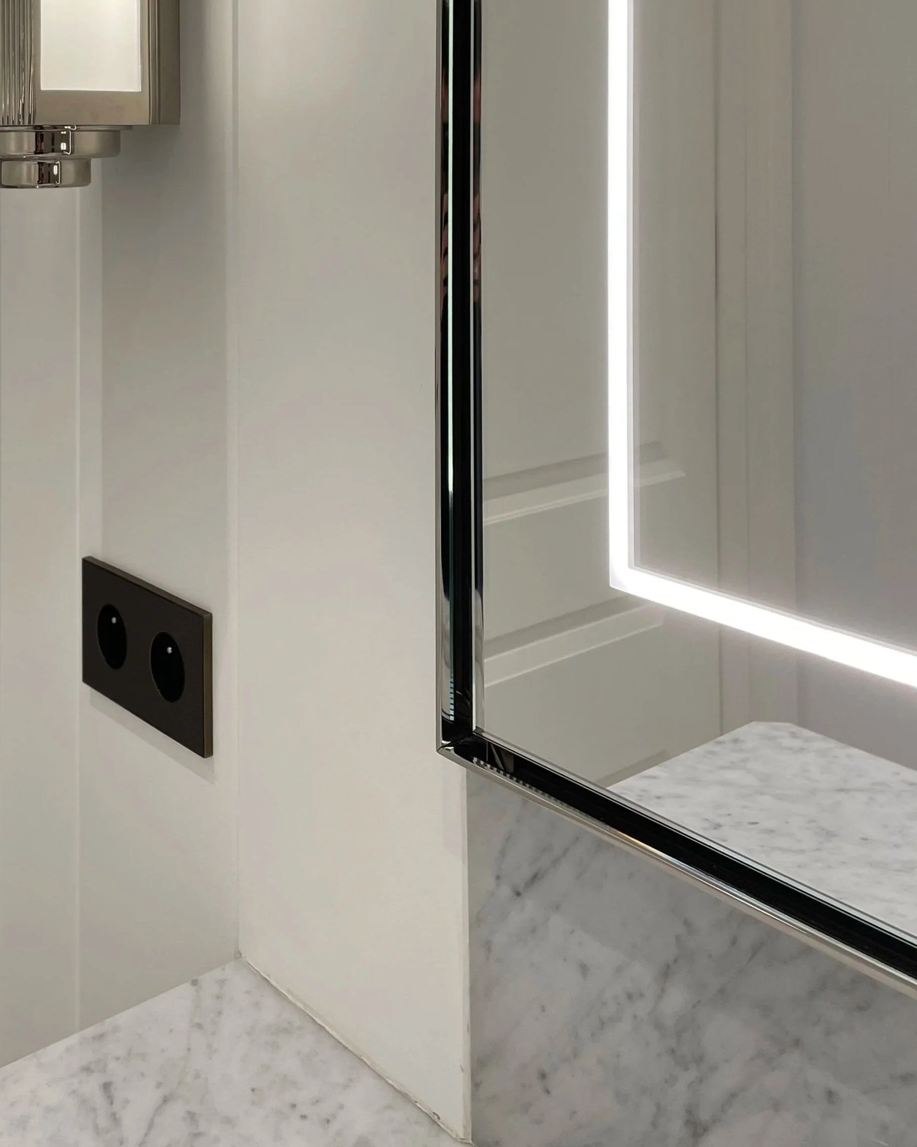 Interno di una stanza da bagno con specchio a LED, piano in marmo e presa elettrica visibile sulla parete.