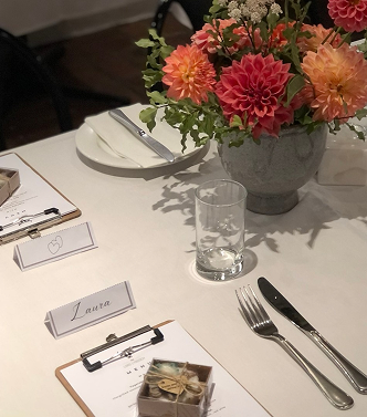Table setting with a floral centerpiece, a glass of water, a plate, cutlery, a name card, and a small gift box.